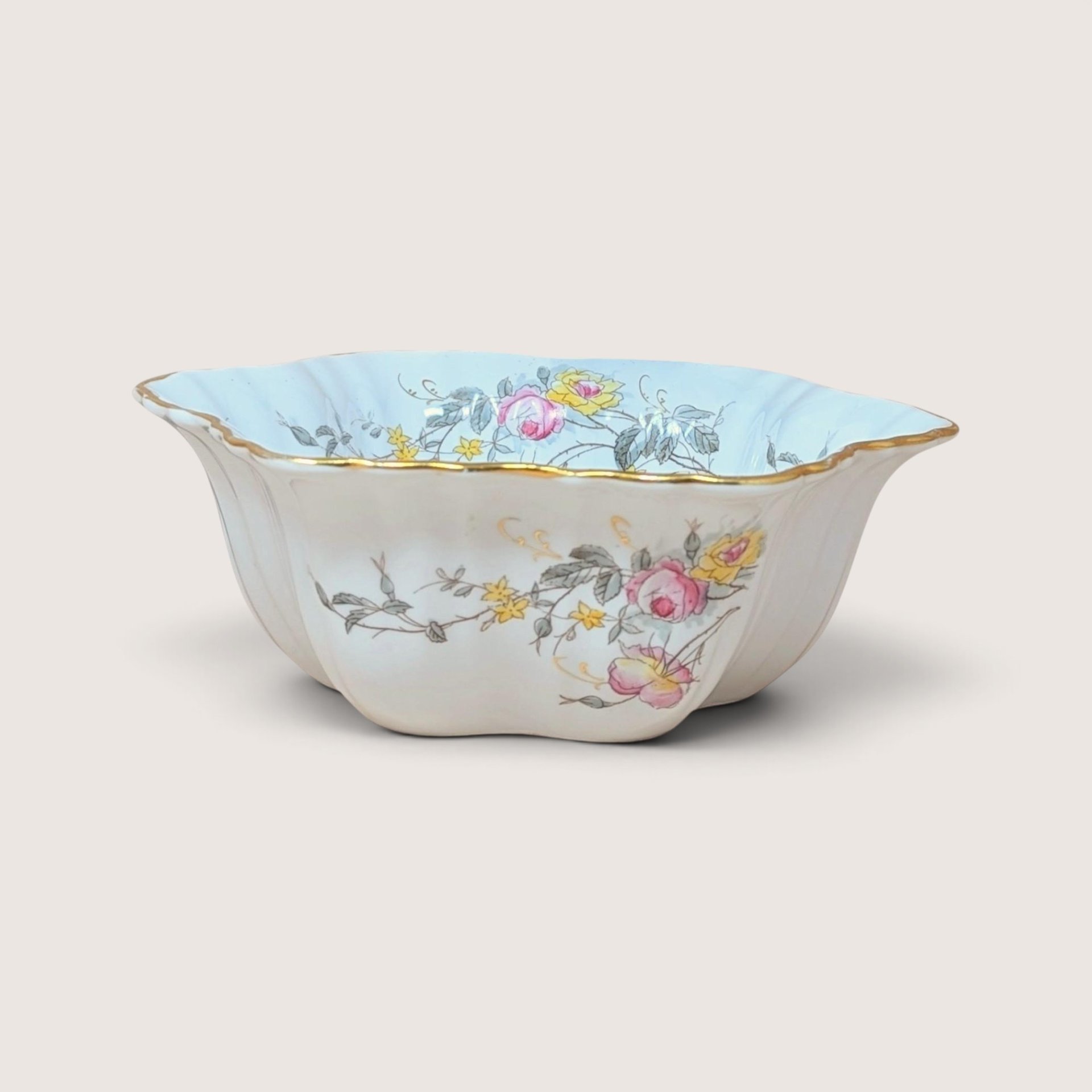 Vintage German porcelain serving bowl featuring a scalloped gold rim and painted pink and yellow floral motifs.