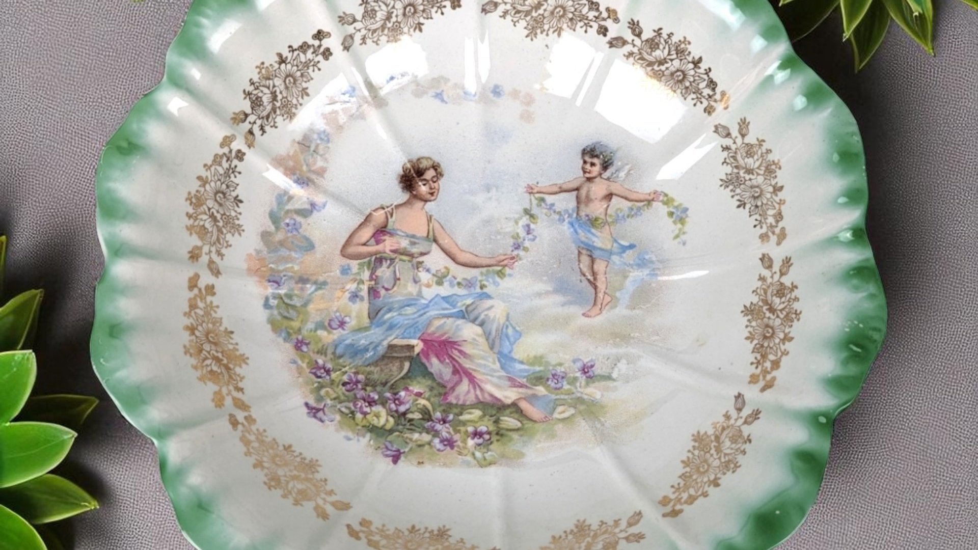 Antique Dresden porcelain bowl with a scalloped edge and green ombré rim. Center features a classical scene of a woman and a cherub with floral garlands. Gold filigree accents. 9.25 inches wide.