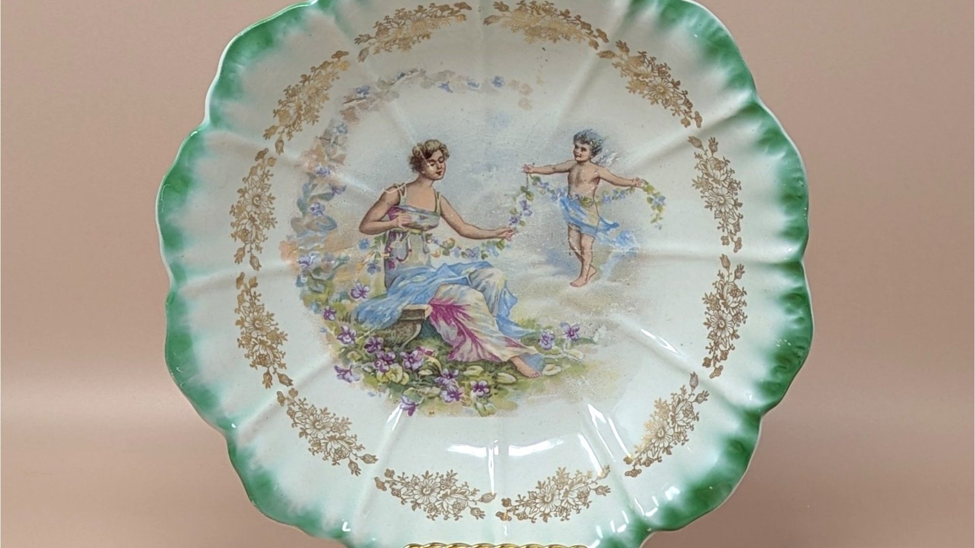 Antique Dresden porcelain bowl with a scalloped edge and green ombré rim. Center features a classical scene of a woman and a cherub with floral garlands. Gold filigree accents. 9.25 inches wide.