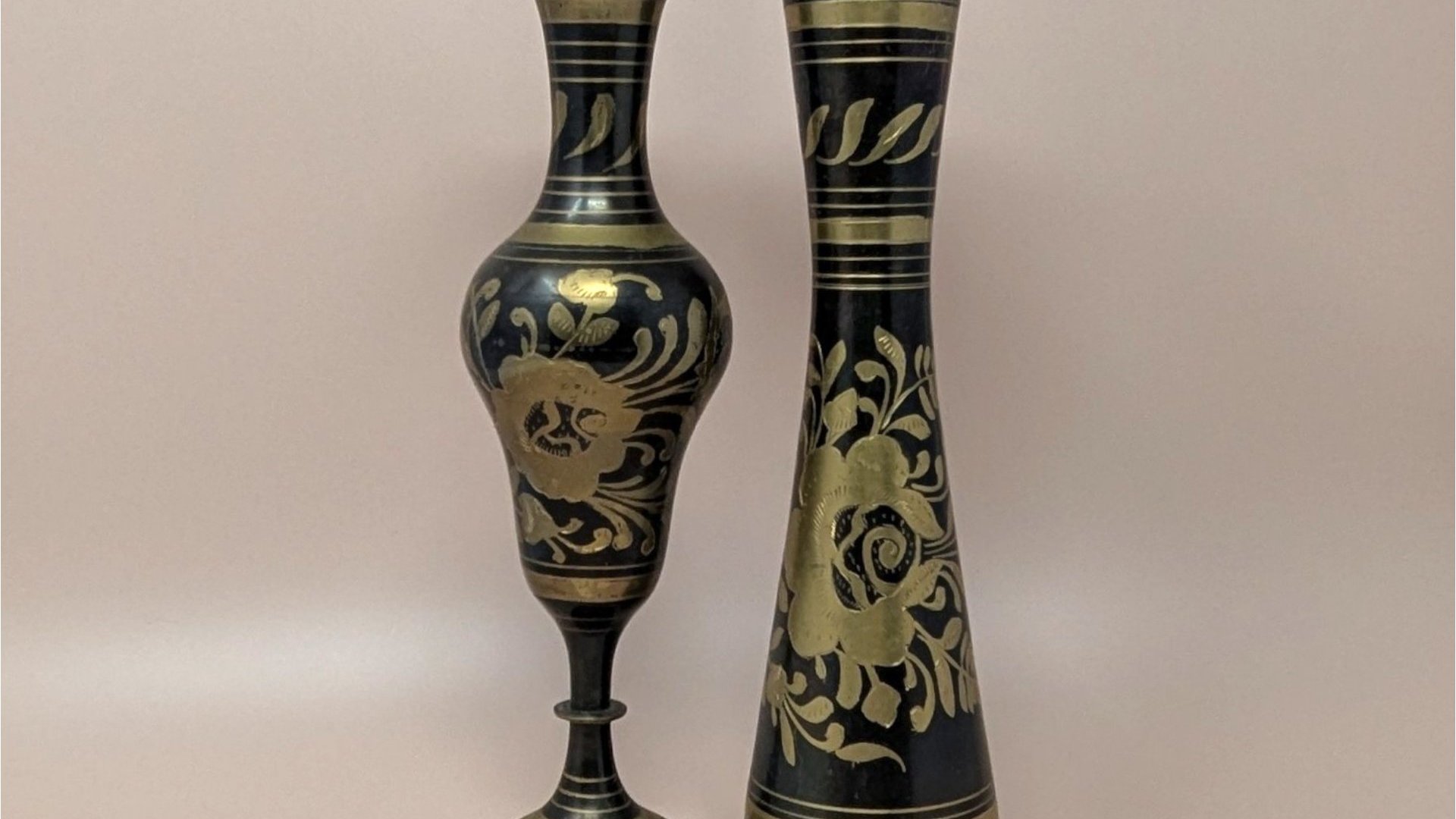 Pair of tall vintage brass vases with a black matte finish. Hand-etched floral designs reveal the golden brass beneath. One is a sleek bud vase; the other features a scalloped rim and a pedestal base. 11.75 inches tall.