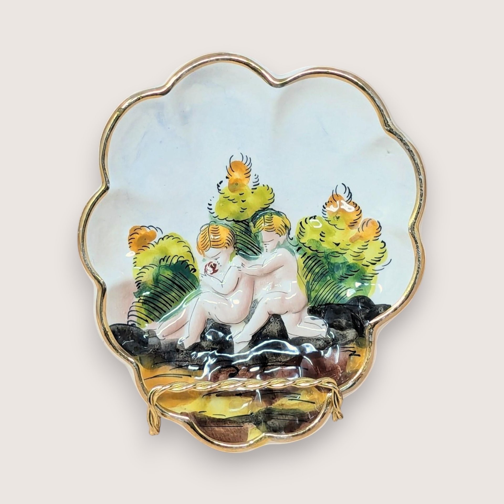 Scalloped Capodimonte porcelain trinket dish with a high-relief embossed scene of two children in a garden. Hand-painted in earthy tones with a gold gilt rim. 5.5 inches wide.