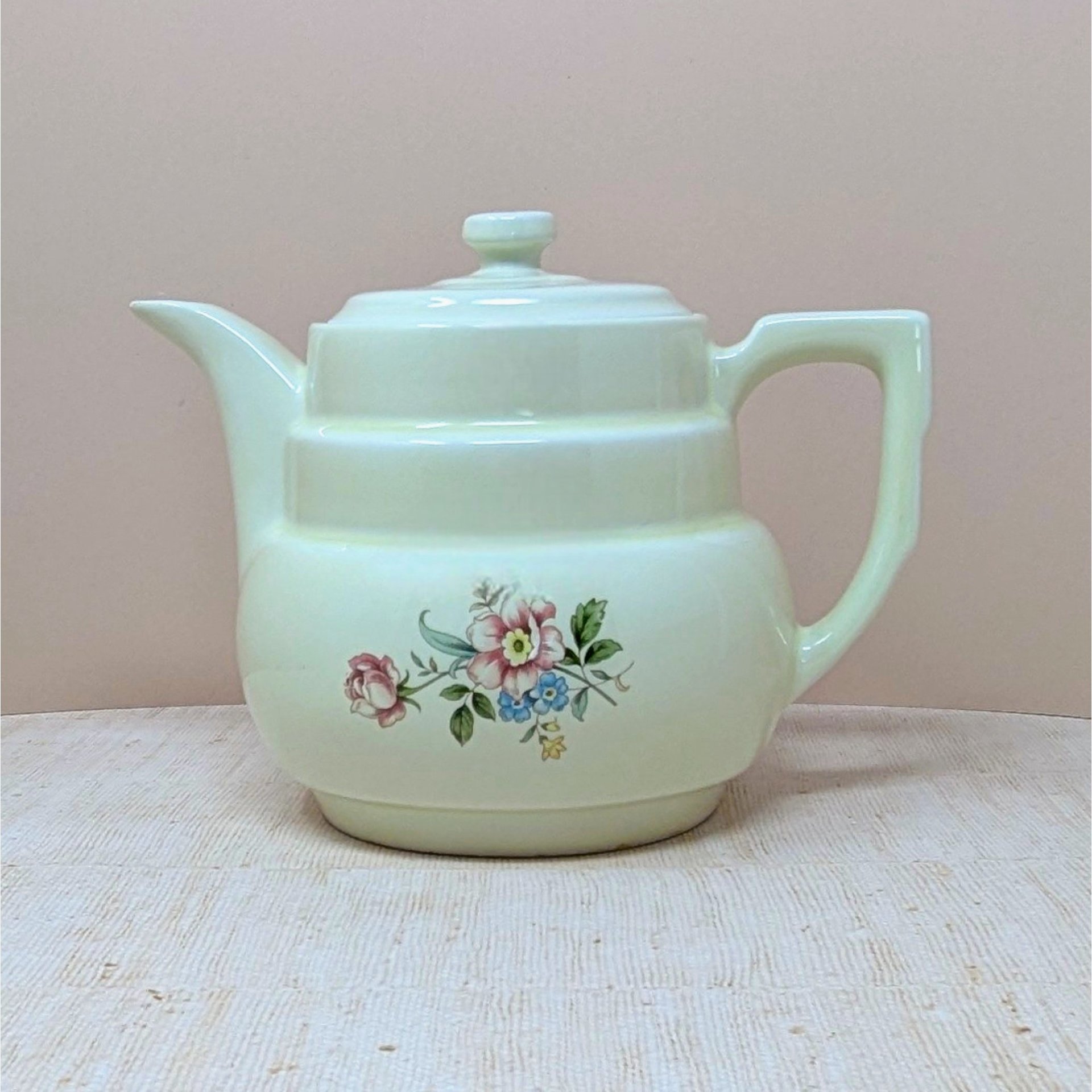 Hall China "Rambling Rose" cream ceramic coffee pot and lid. Features a tiered Art Deco body, an angular handle, and a delicate pink and blue floral spray. 7.75 inches tall.