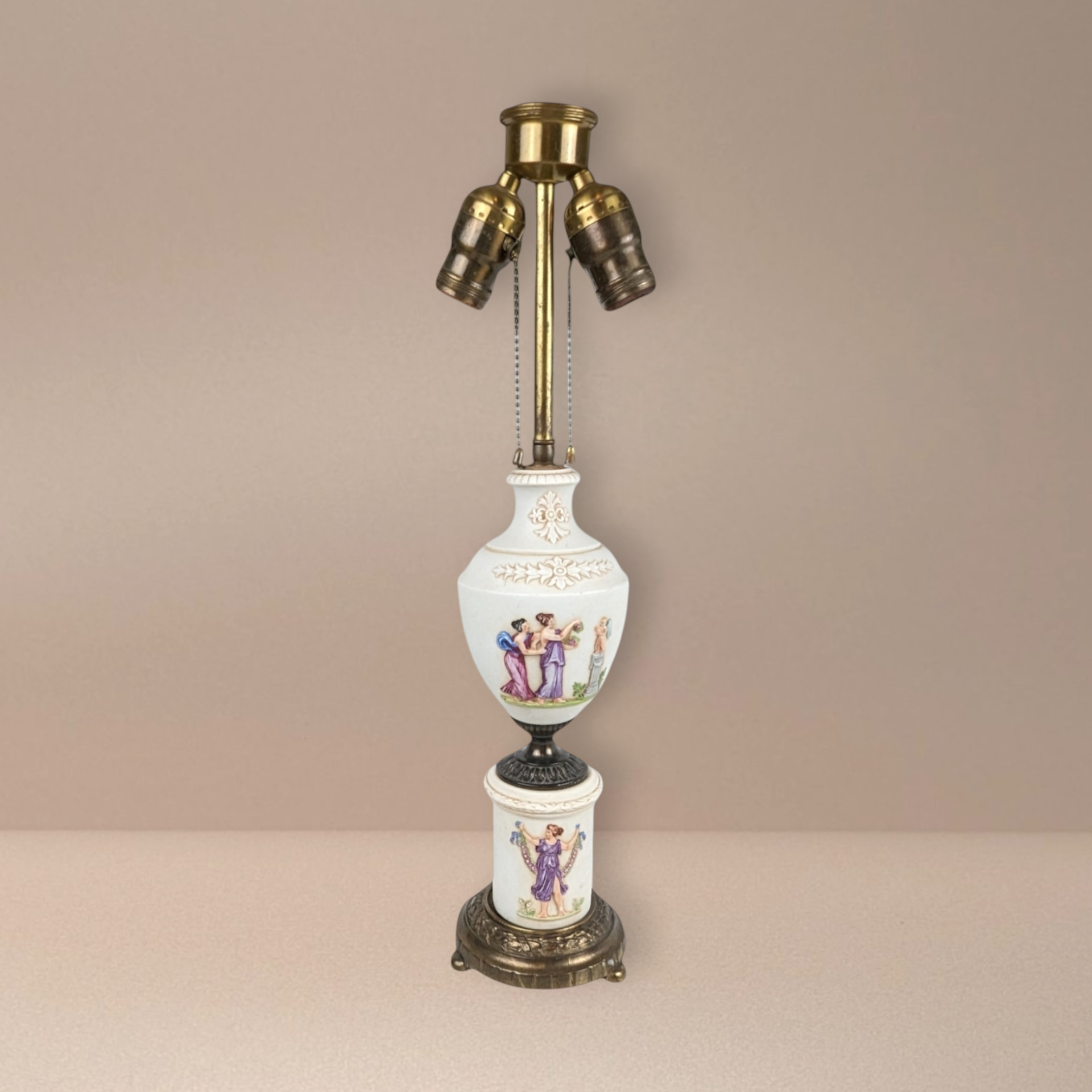 Tall antique Capodimonte-style porcelain lamp. Features high-relief classical figures of nymphs and cherubs. Cream body with gold gilt accents on an ornate brass base. Double pull-chain socket. 19 inches tall.