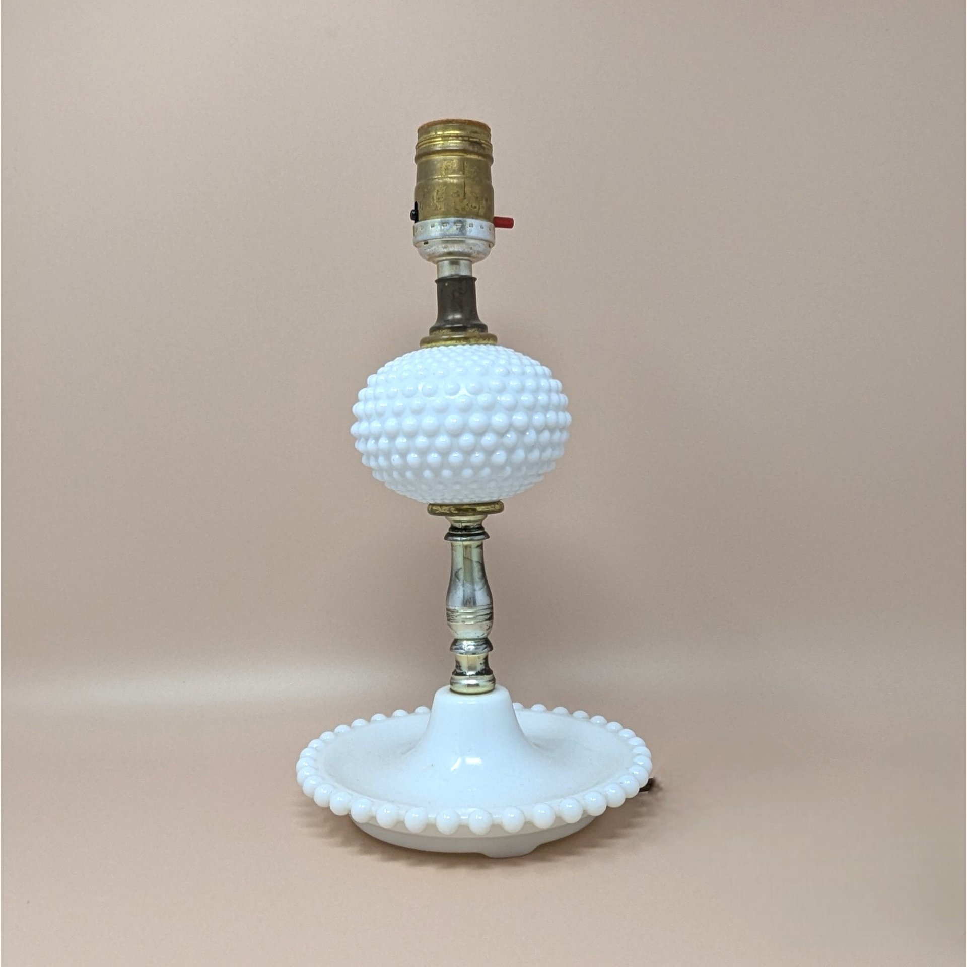 Vintage white milk glass lamp with a hobnail texture. Features a central hobnail globe and a wide, beaded tray base. Brass-tone hardware. 11.5 inches tall.