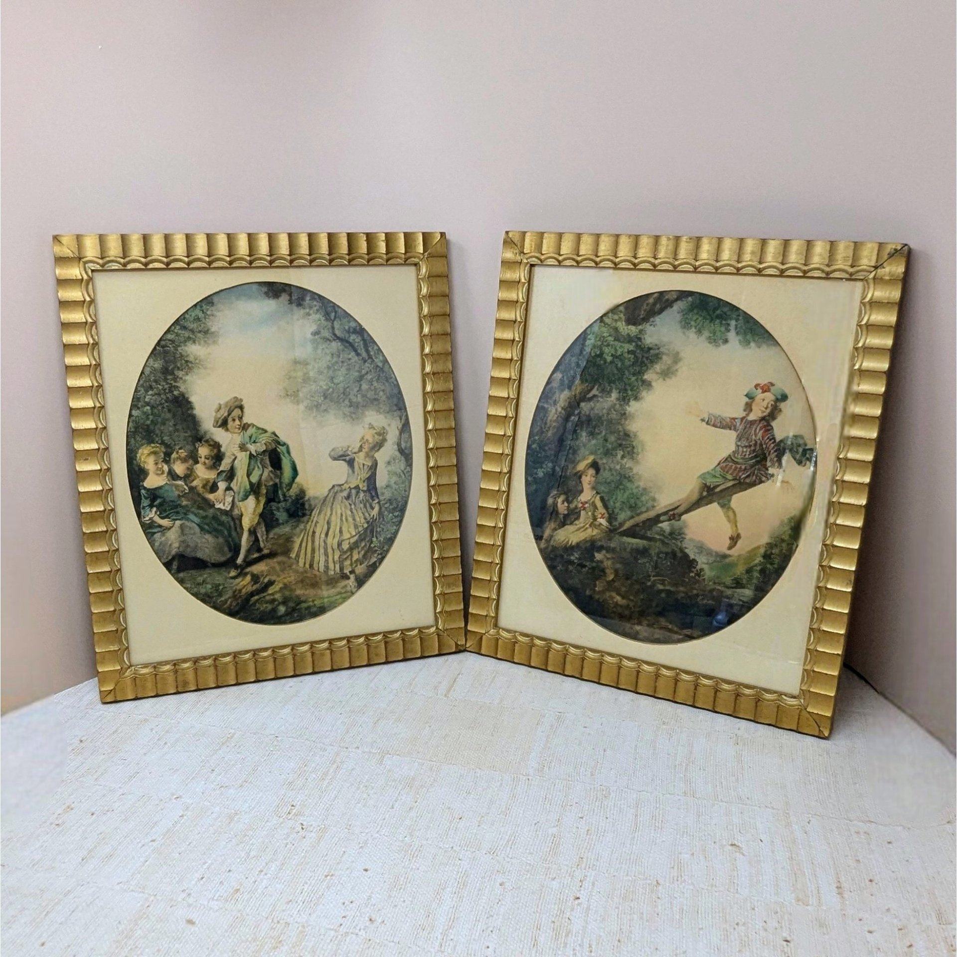 Set of two 1940s framed art prints by Nicolas Lancret titled "The Seesaw" and "Dropping the Handkerchief." Features pastoral Rococo scenes in ornate scalloped gold frames. 14.25 x 12.25 inches.