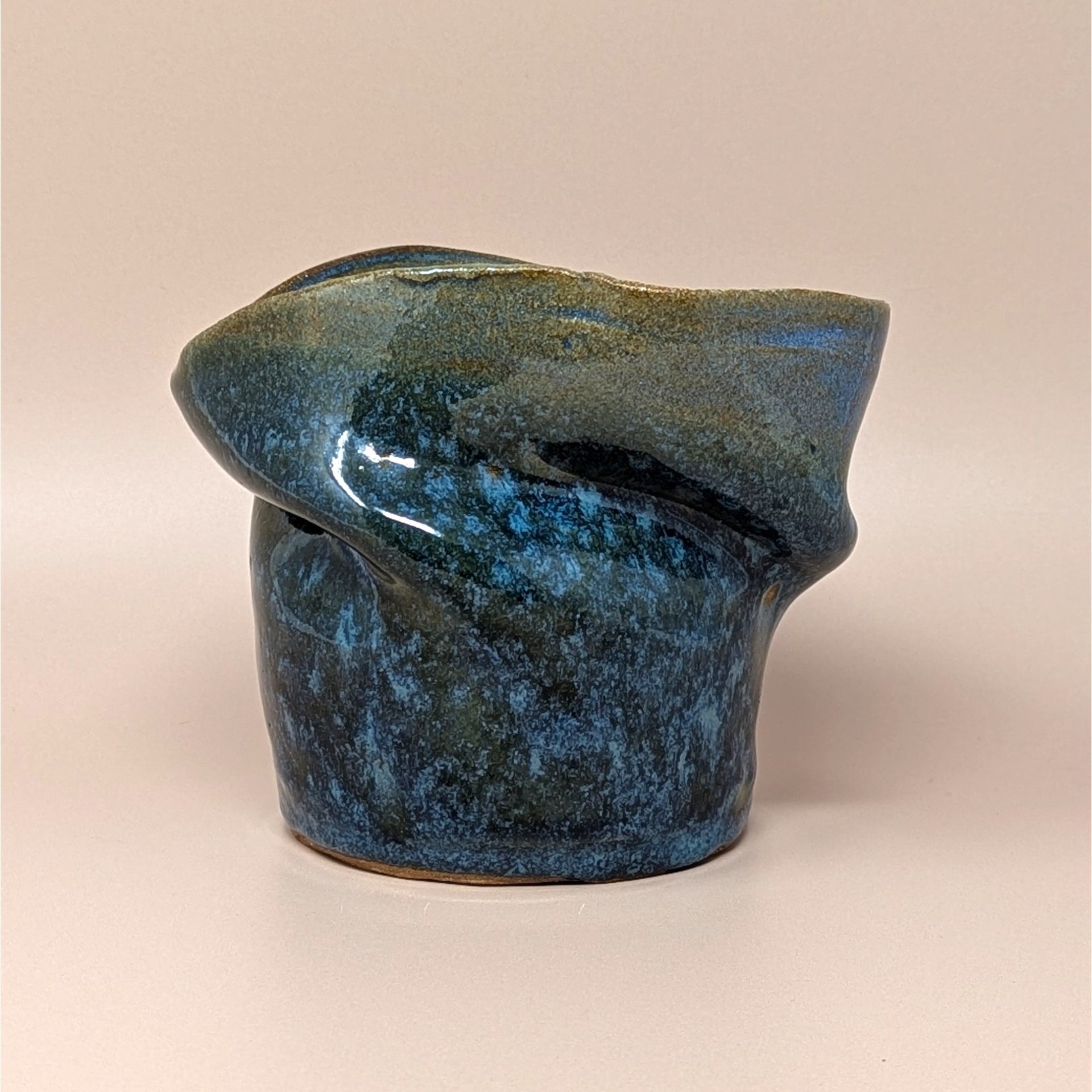 Vintage handmade studio pottery vase with an asymmetrical, pinched silhouette. Features a mottled deep blue and earth-toned glaze with a high-gloss finish. Signed on the base. 5 inches tall.