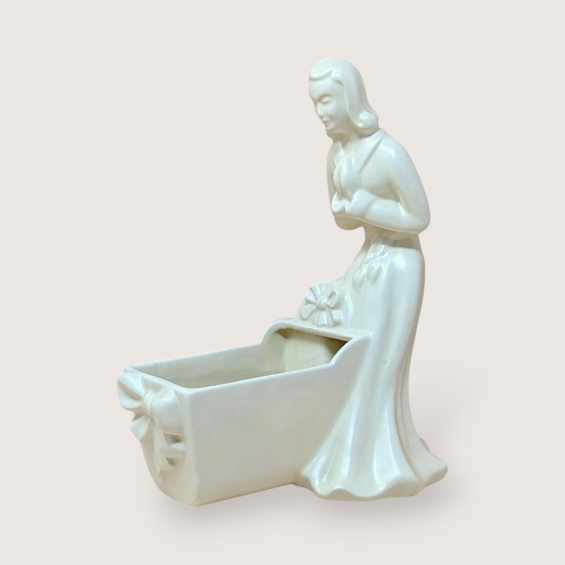 Vintage Royal Haeger white pottery planter featuring a colonial-style woman in a flowing dress leaning over a baby cradle. High-gloss "Alabaster" white glaze. 11 inches tall.