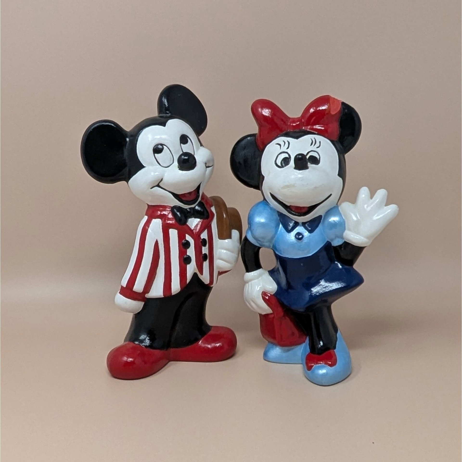Set of two vintage 9-inch hand-painted Disney figurines. Dapper Mickey in a red-and-white striped jacket holding a brown hat. Minnie in a blue dress and red bow waving. Ceramic style.