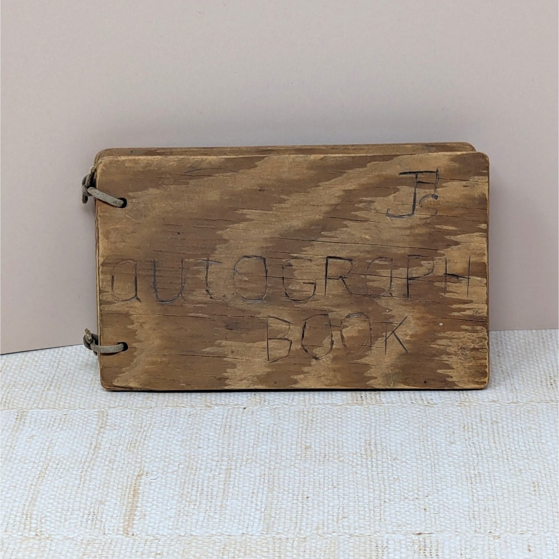 A small, rectangular autograph book with a natural wood grain cover. The words "Autograph Book" are hand-carved into the wood. Two metal rings bind the pages on the left. Rustic, weathered texture with a warm honey-oak finish.