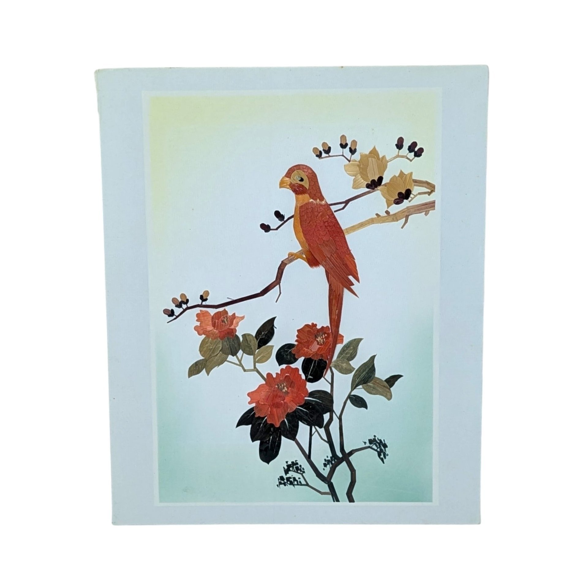A vertical rectangular wall art piece featuring a bird perched on a branch, meticulously crafted from layered bamboo. Warm sienna and ochre tones are accented by deep red floral blooms. Framed with a clean white and pink double mat.