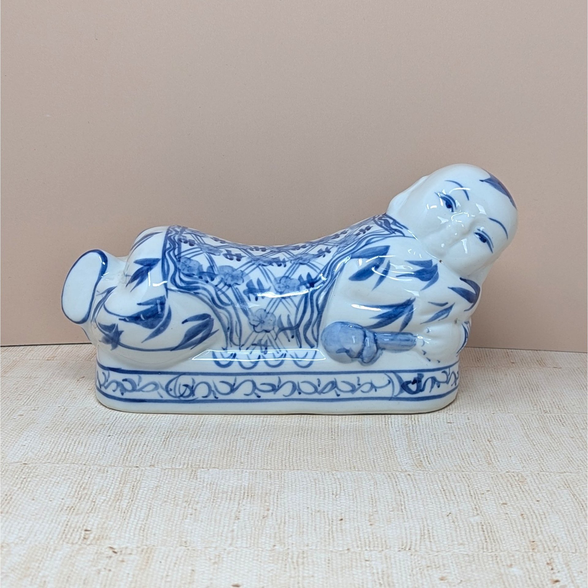 A horizontal porcelain headrest shaped like a reclining child. Featuring a crisp white ground with traditional cobalt blue floral and scroll patterns. Glossy vitrified texture with hand-painted facial details.