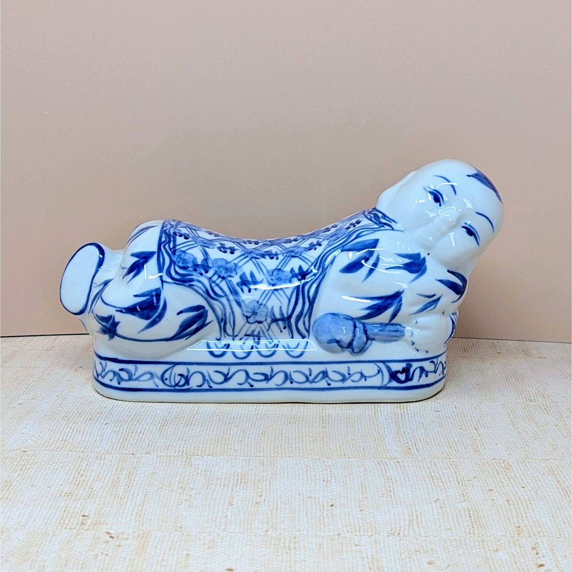 A horizontal porcelain headrest shaped like a reclining child. Featuring a crisp white ground with traditional cobalt blue floral and scroll patterns. Glossy vitrified texture with hand-painted facial details.