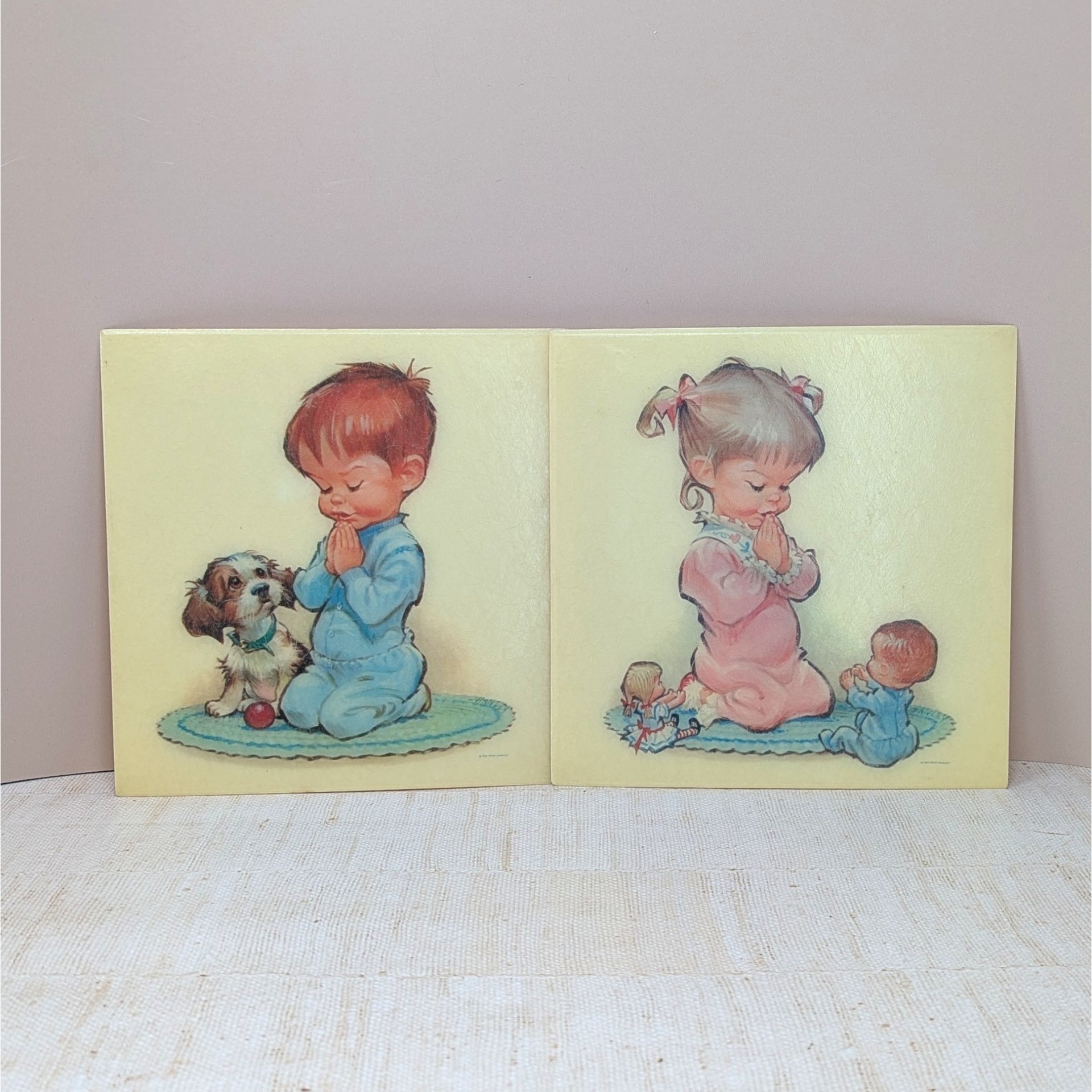 A pair of square fiberglass wall plaques with cream backgrounds. One features a young girl in pink pajamas praying, and the other shows a boy in blue pajamas praying with a small puppy. Soft, mid-century illustrated style.