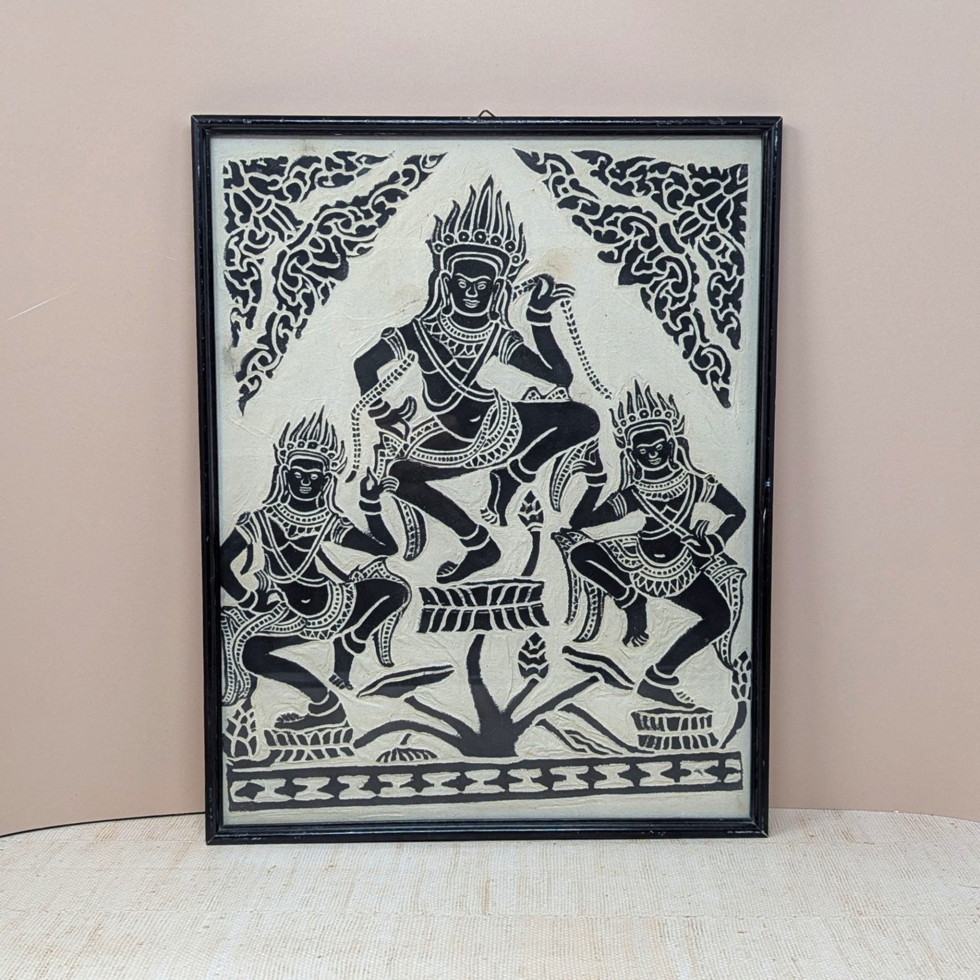 A vertical framed art piece on textured rice paper featuring three Apsara dancers in traditional Cambodian headdresses and poses. Bold black ink on a cream-white background. Framed in a minimalist black wood frame.