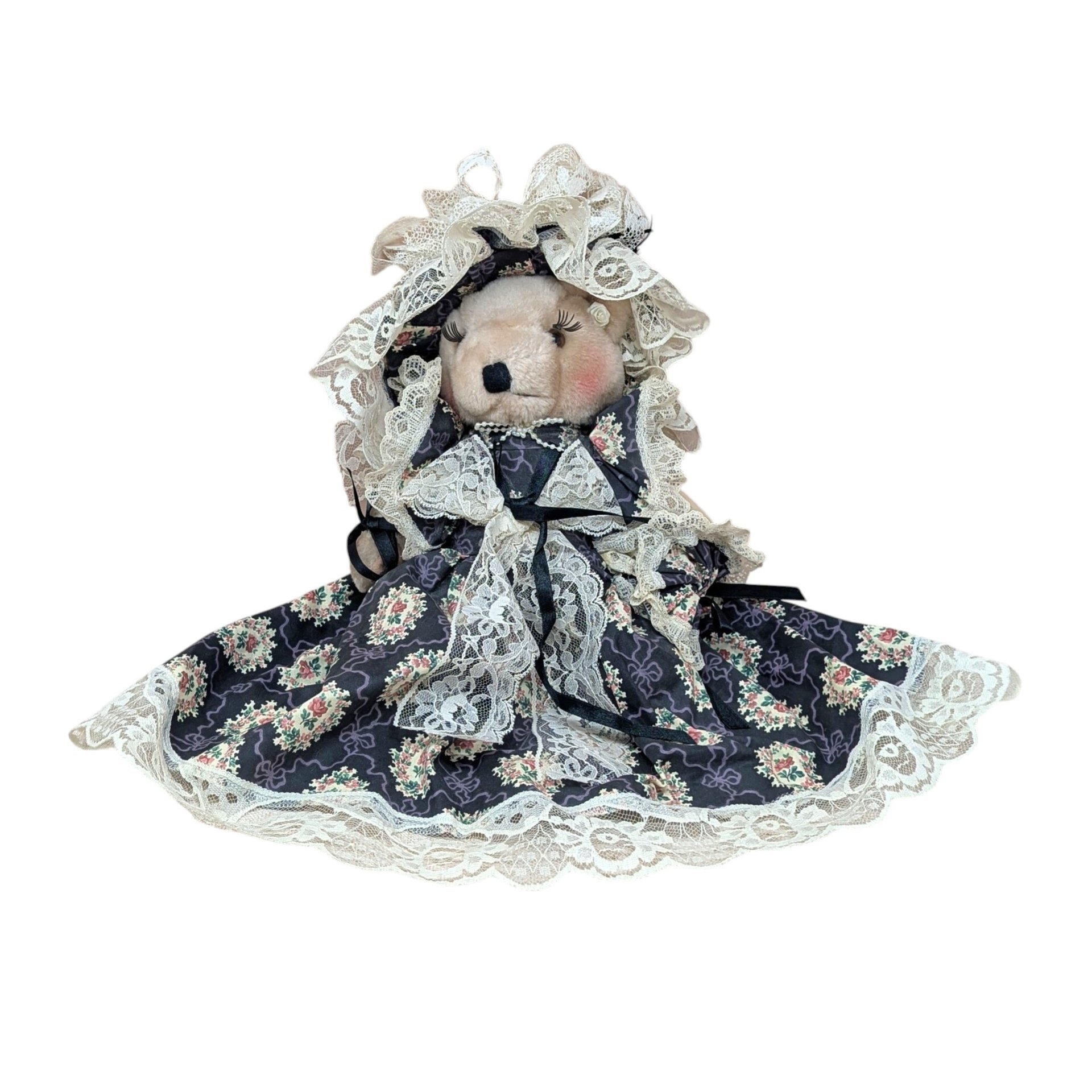 A vertical 12-inch handcrafted teddy bear with tan fur and movable limbs. Wearing an elaborate Victorian-style dark floral dress with voluminous cream lace trim and a matching oversized lace bonnet.