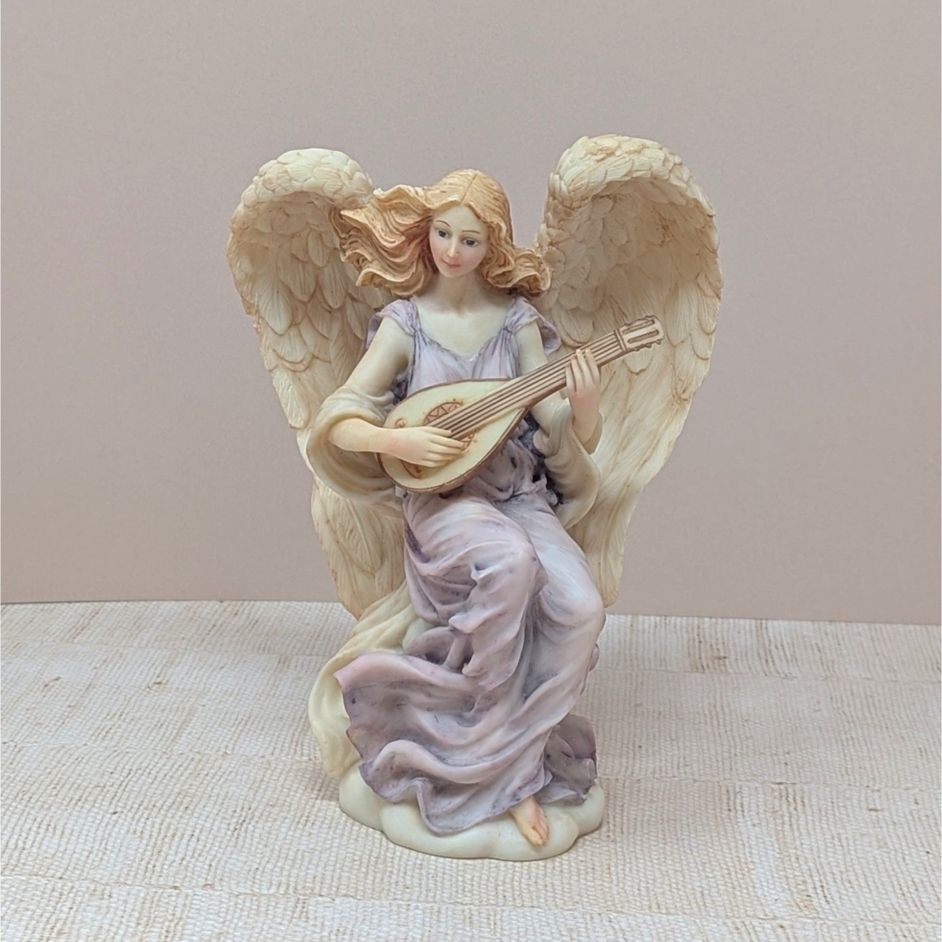 A vertical 7-inch resin figurine of a winged angel named Lydia. She wears flowing mauve robes and is depicted playing a lute-like instrument. The wings are highly detailed with a soft peach-cream finish. Includes original Roman Inc. gold tag.