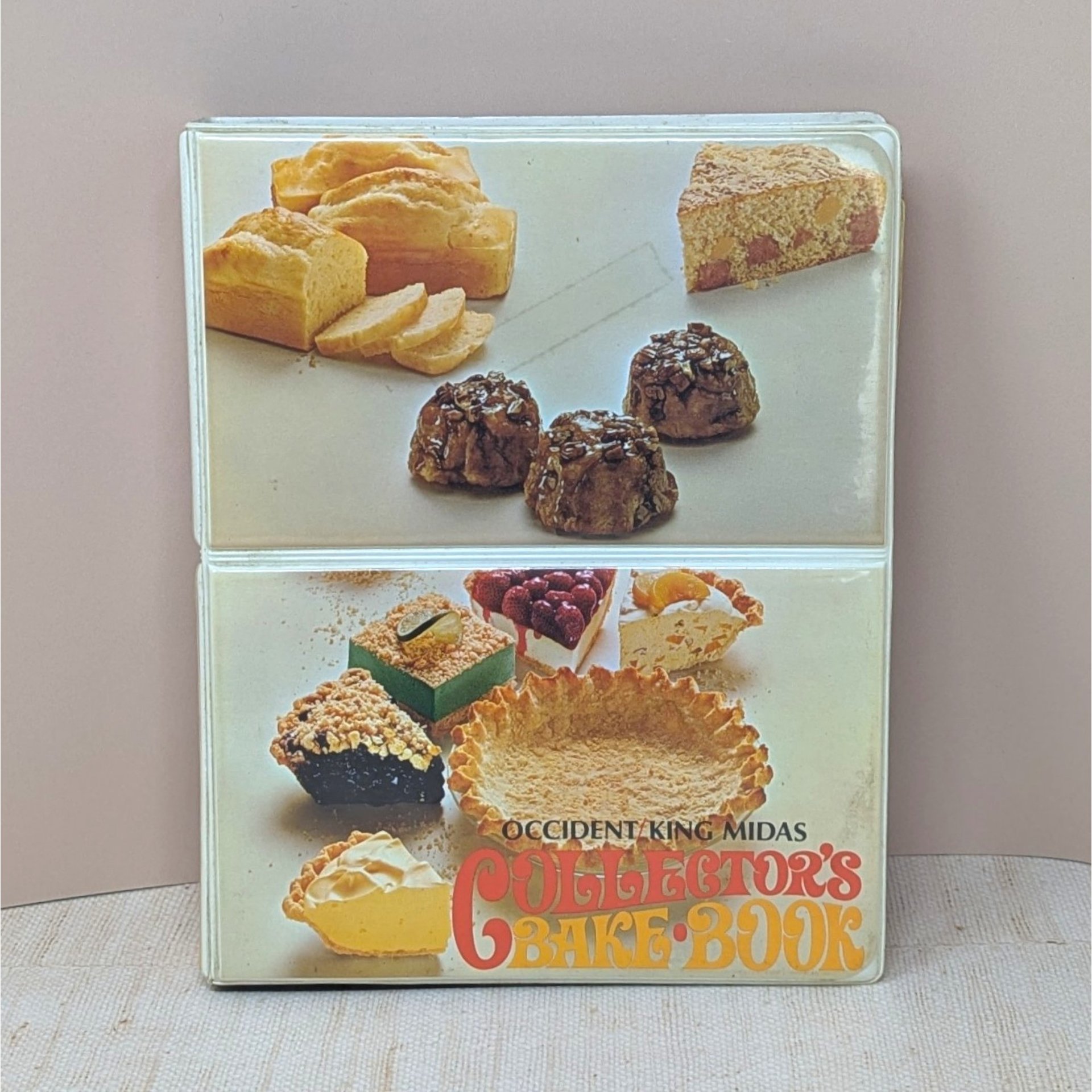 A vertical cookbook titled "Occident King Midas Collector's Bake Book." The cover features two panels of 1970s food photography showing pies, cakes, and breads. Orange and yellow "bubble" style typography.