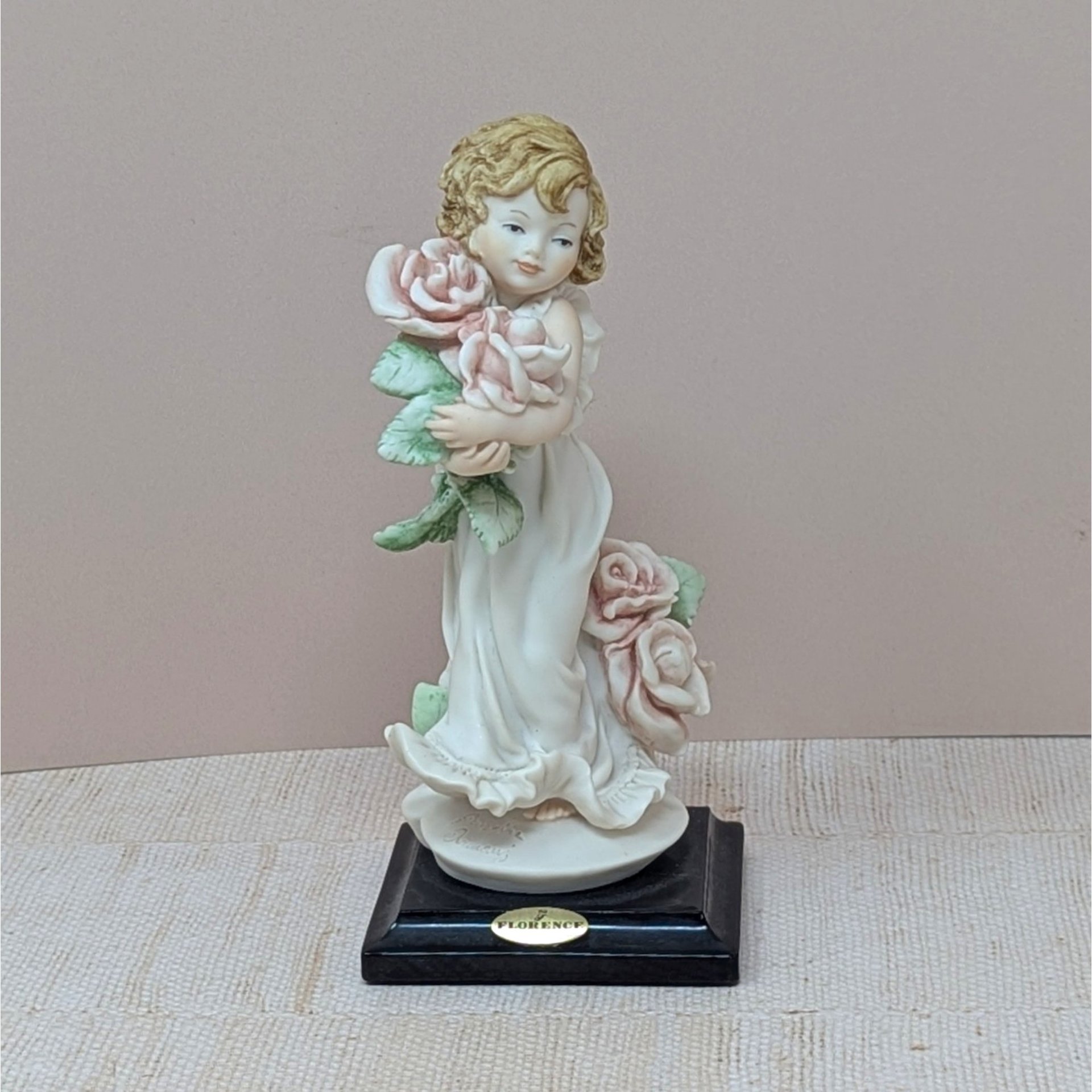 A finely detailed porcelain figurine of a young girl in a flowing white dress holding a large bouquet of pink roses. She stands on a dark wooden base with a gold Florence Giuseppe Armani plaque.