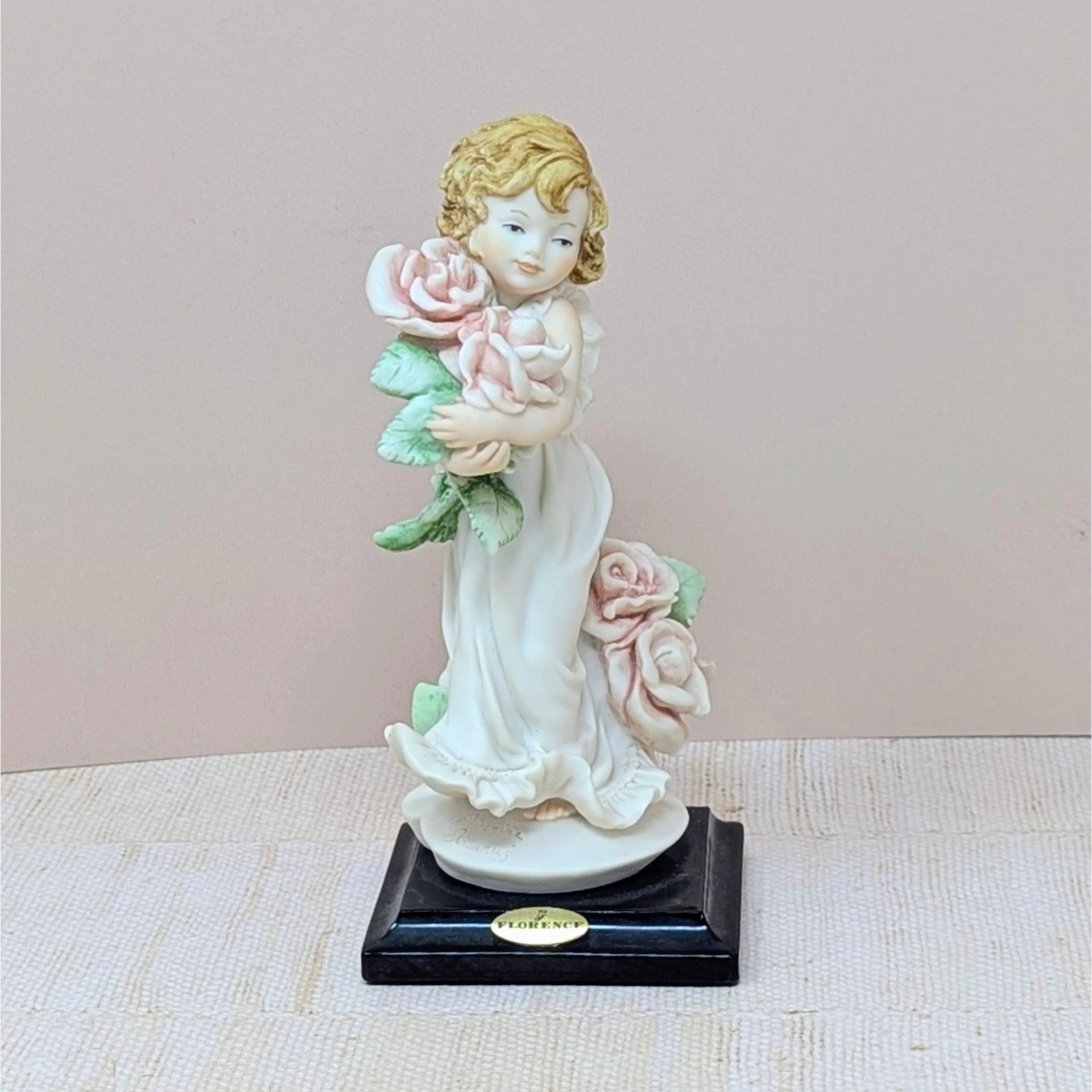 A finely detailed porcelain figurine of a young girl in a flowing white dress holding a large bouquet of pink roses. She stands on a dark wooden base with a gold Florence Giuseppe Armani plaque.