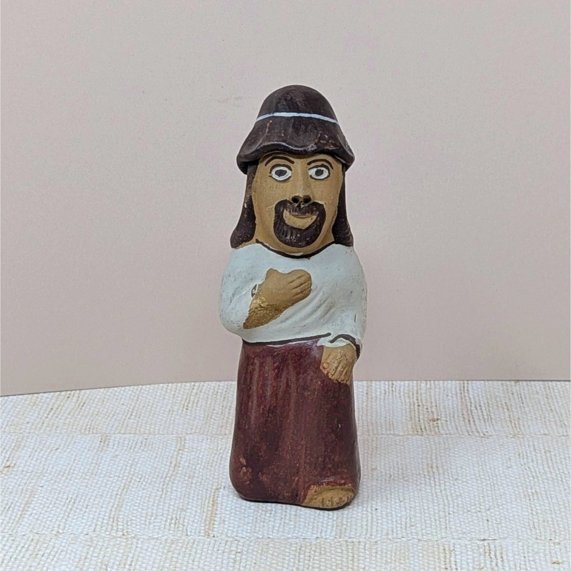 A hand-painted clay figurine of a bearded man with a hat and a white tunic. The figure is hollow with small holes for use as a whistle or ocarina. 6 inches tall.