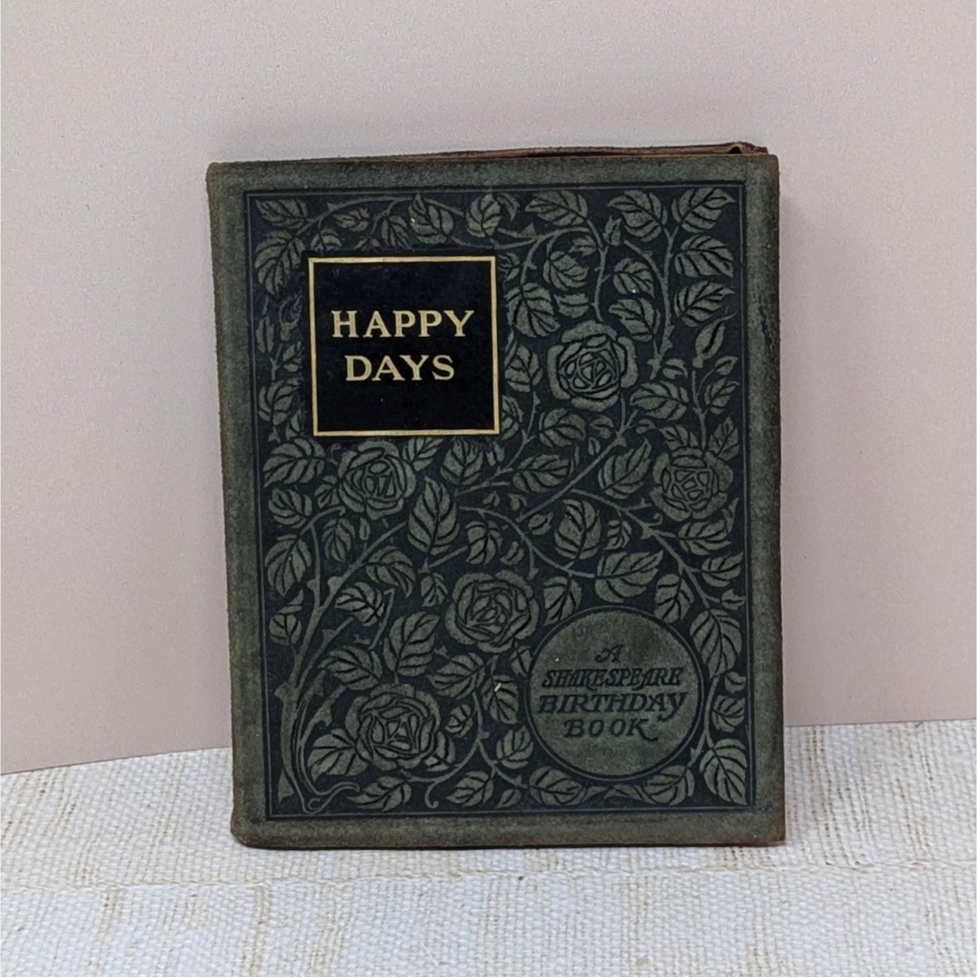 A small, 1904 leather-bound book titled "Happy Days: A Shakespeare Birthday Book." The dark cover is intricately embossed with a floral rose pattern and gold-foil lettering, showing a soft, aged patina on the edges.