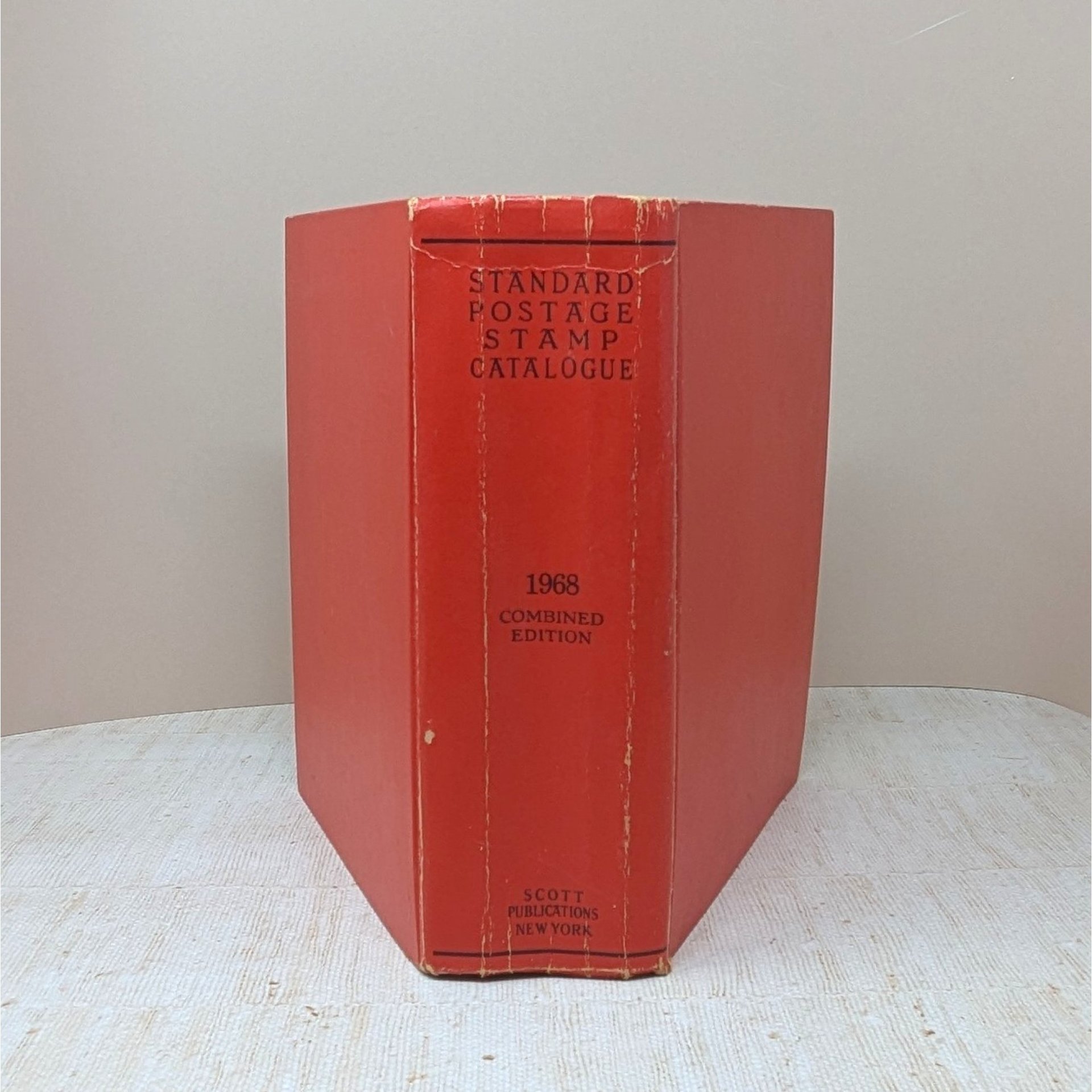 A thick, red hardcover book with a textured spine. The text reads Standard Postage Stamp Catalogue 1968 Combined Edition in black ink. The cover shows gentle edge wear and a slight lean from its substantial page count.