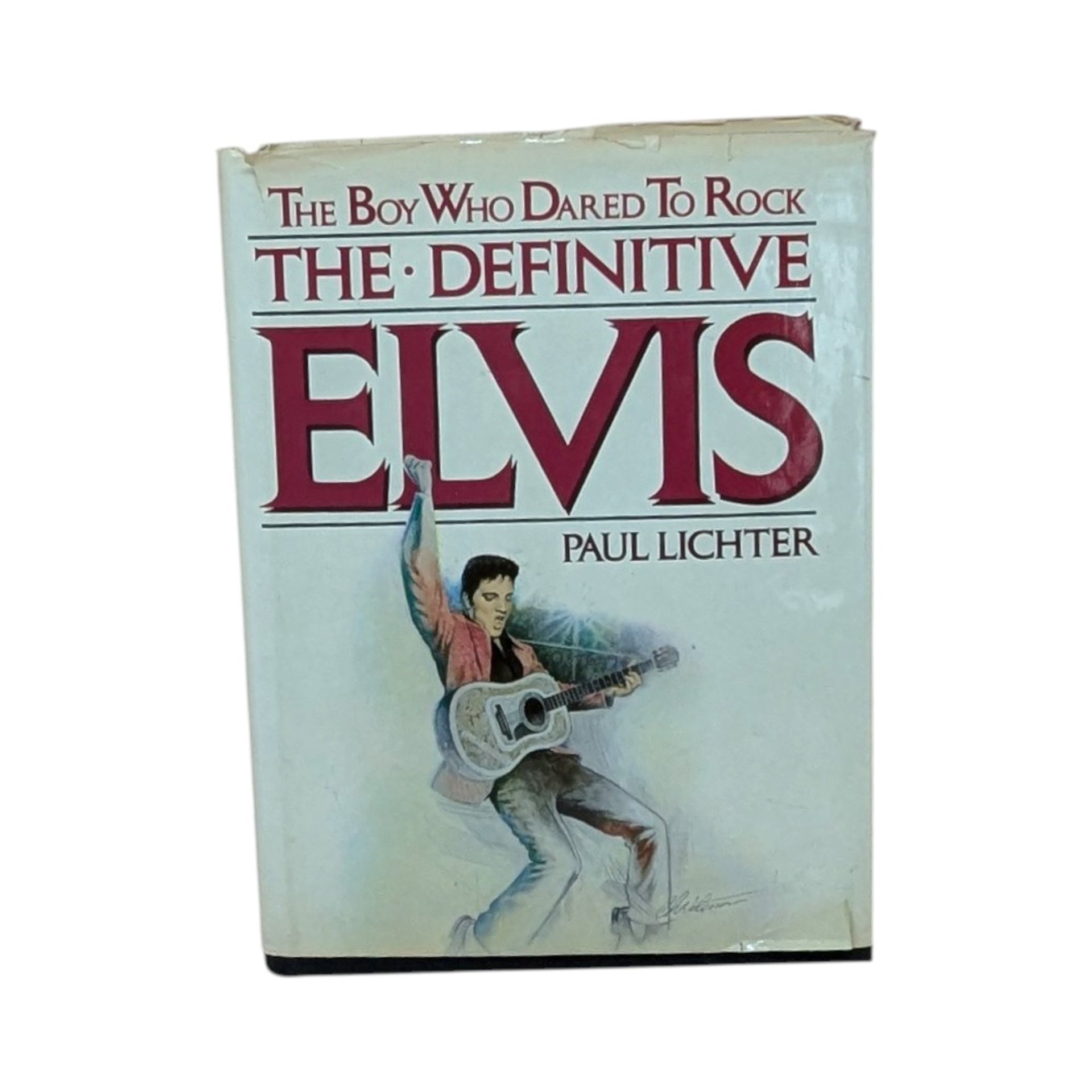 A large hardcover book titled The Boy Who Dared To Rock: The Definitive Elvis. The white dust jacket features an illustration of Elvis Presley in a pink jacket with a guitar. The jacket shows visible edge wear and small tears.