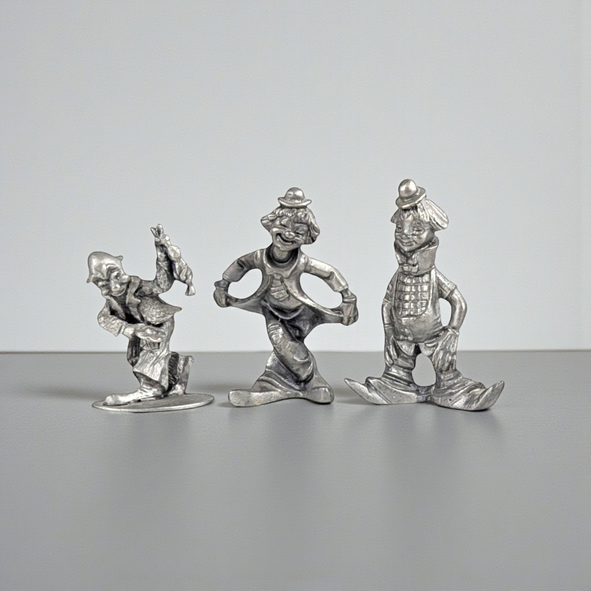 A set of three vintage silver-toned pewter clown figurines in different poses, including one bowing in a curtsy, one standing with hands in pockets, and one in a playful walking stance.