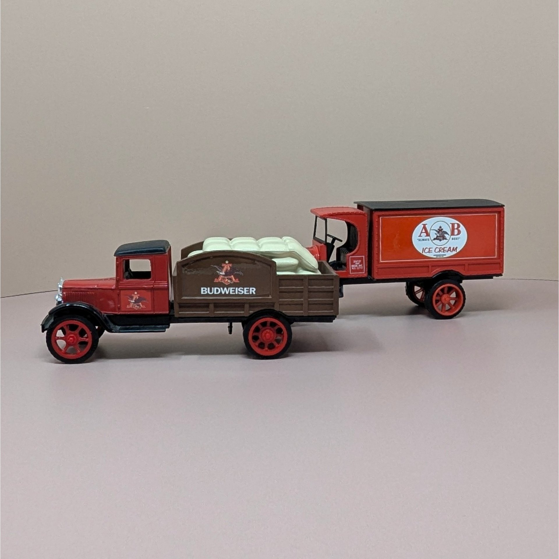 Two vintage red and brown die cast metal Anheuser Busch delivery truck banks. One is a flatbed carrying white yeast sacks, the other is an A and B Ice Cream panel truck.