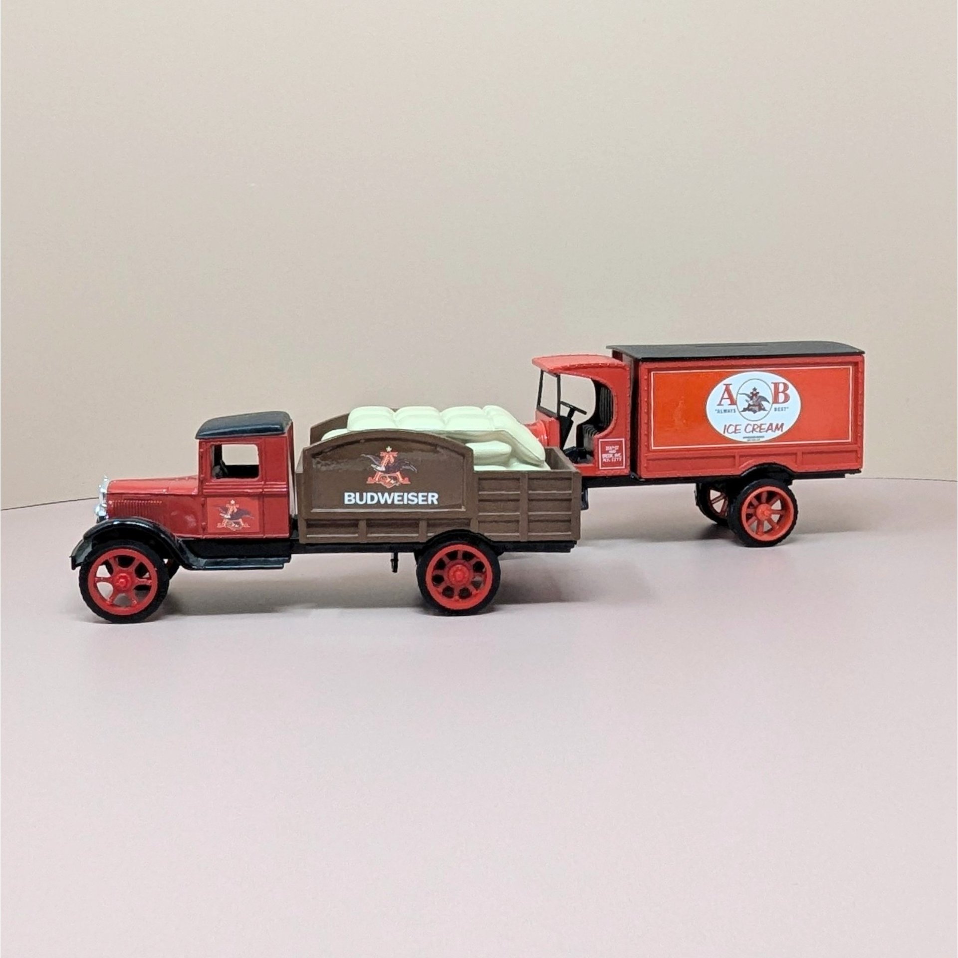 Two vintage red and brown die cast metal Anheuser Busch delivery truck banks. One is a flatbed carrying white yeast sacks, the other is an A and B Ice Cream panel truck.