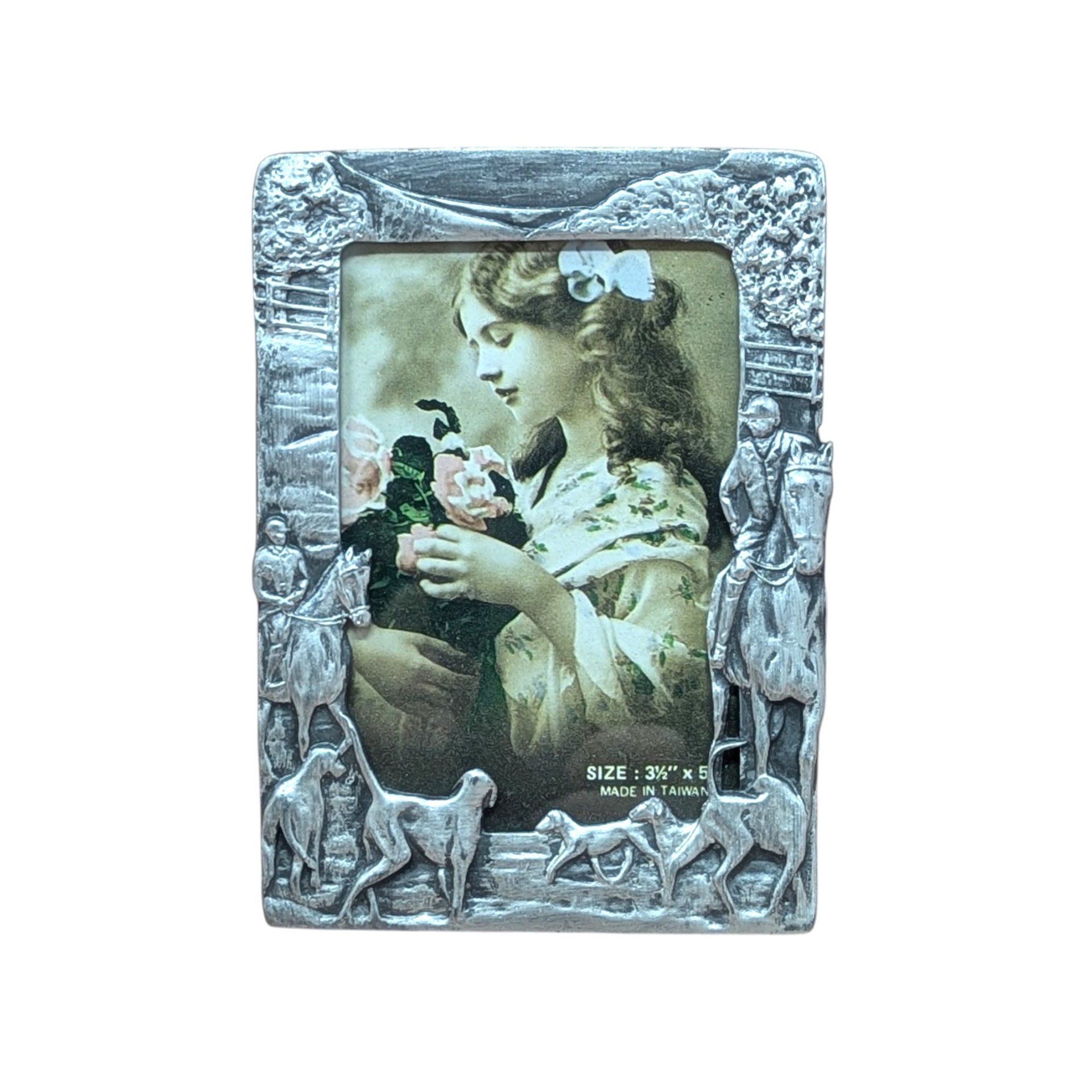 A vertical cast-metal picture frame with a weathered silver finish. Embossed hunters on horses and a pack of running hounds frame a portrait of a young girl with flowers.
