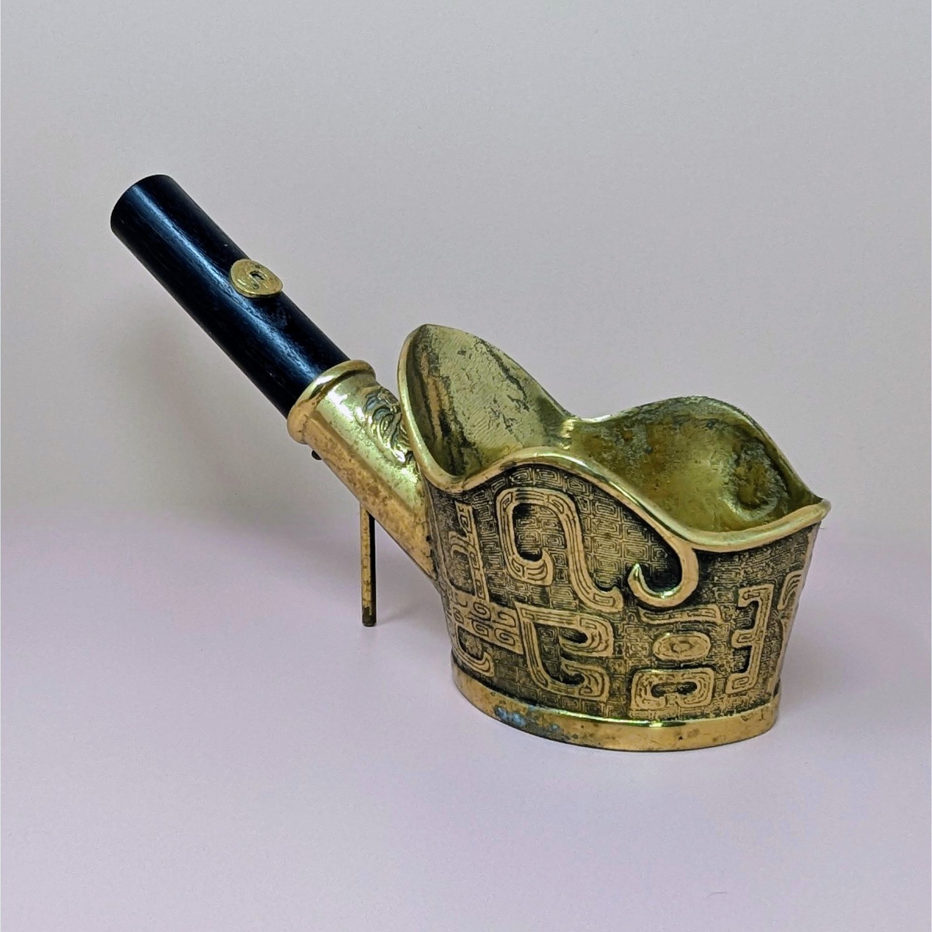 Brass silk iron with a long black wooden handle and ornate etched patterns on the vessel, shown on a neutral background.