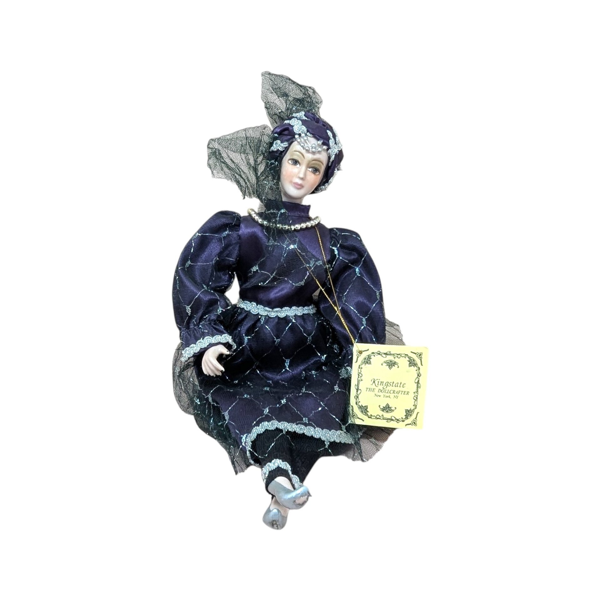 A vintage Kingstate porcelain harlequin doll in a deep purple satin dress with silver lattice patterns and lace trim. She features hand-painted facial features and an ornate turban with a black mesh veil.