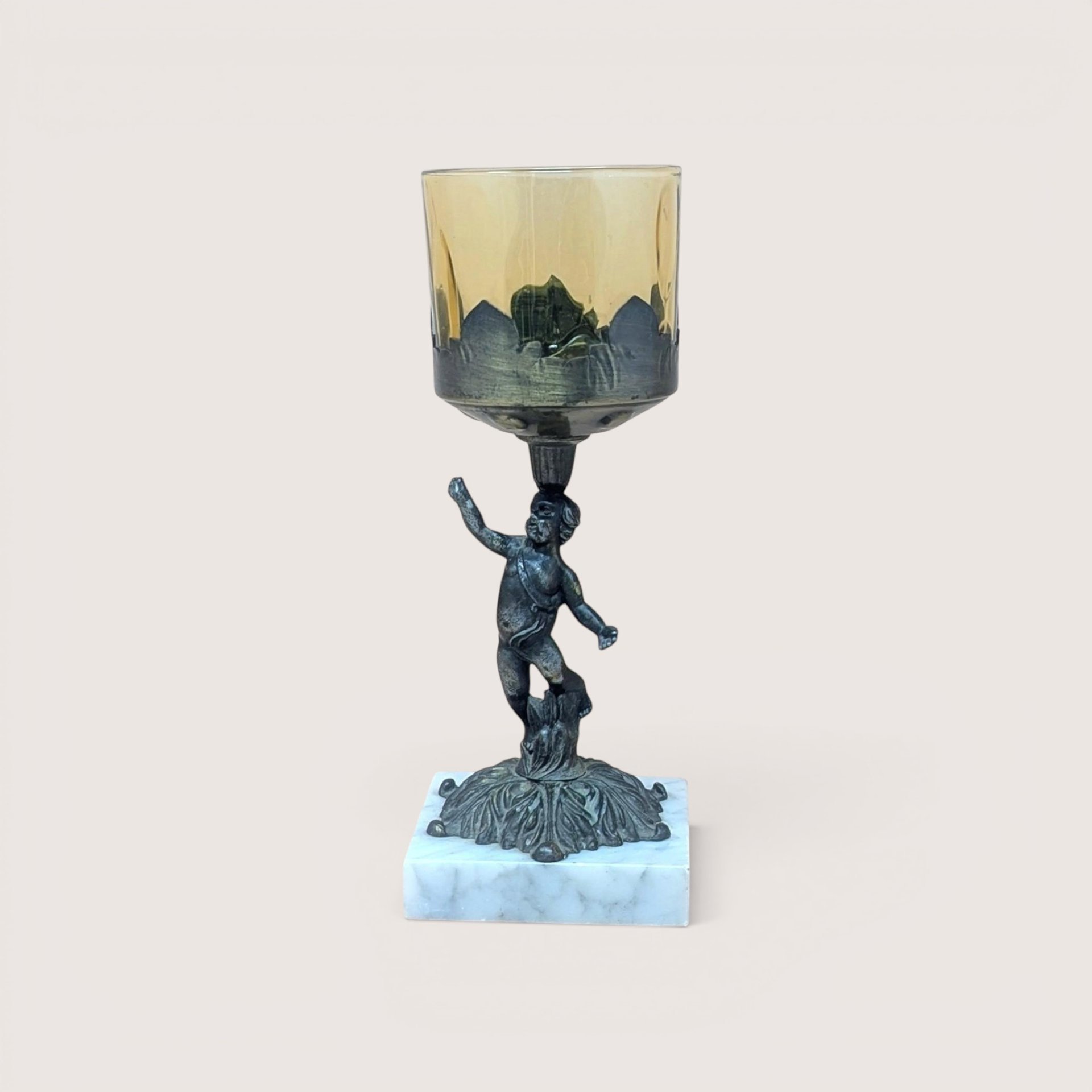 A 9-inch vintage candle holder featuring a dark cast metal cherub figure standing on a white marble square base, supporting a translucent amber glass cup.