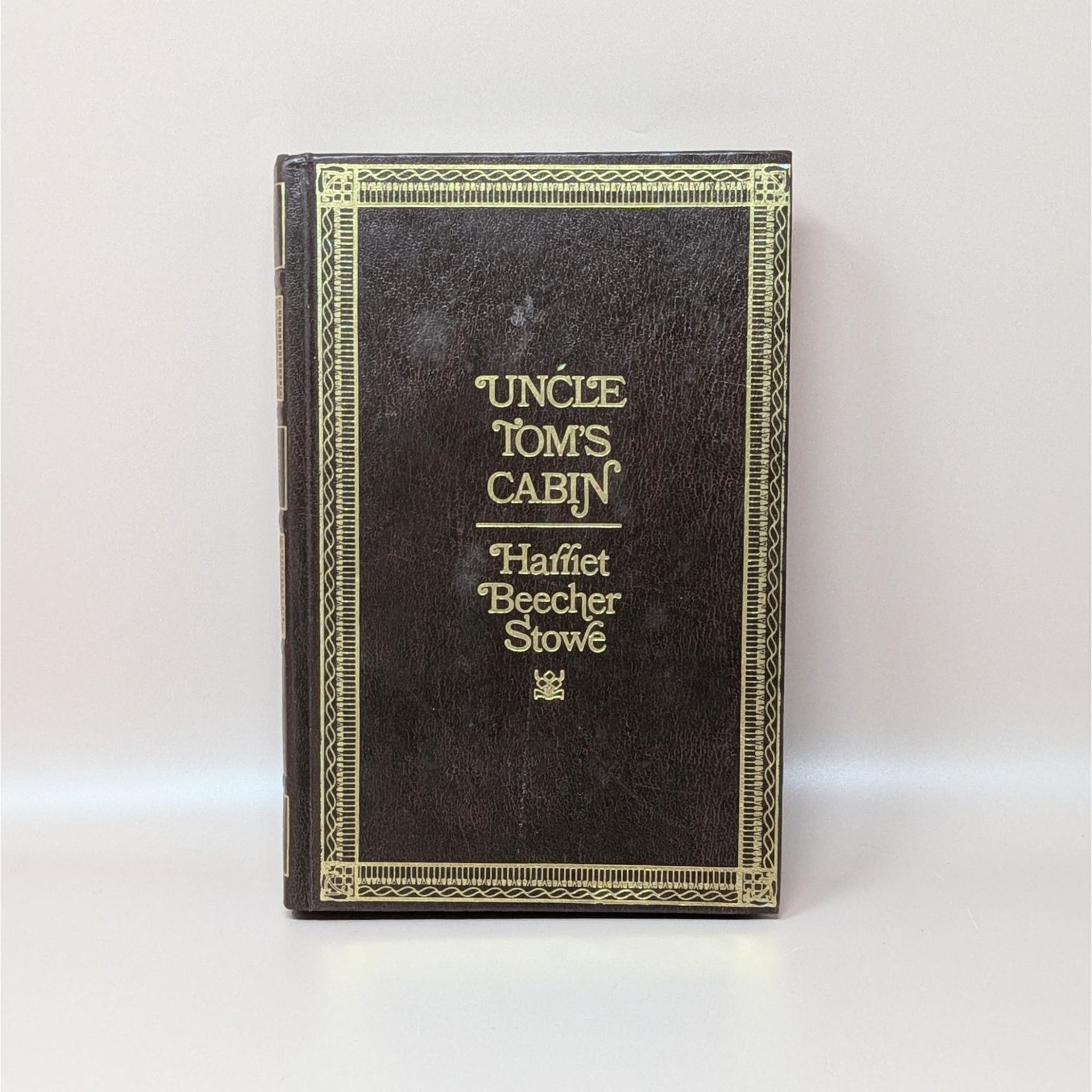 A 1976 hardcover edition of Uncle Tom's Cabin by Harriet Beecher Stowe with a dark brown textured cover and gold gilt lettering and borders