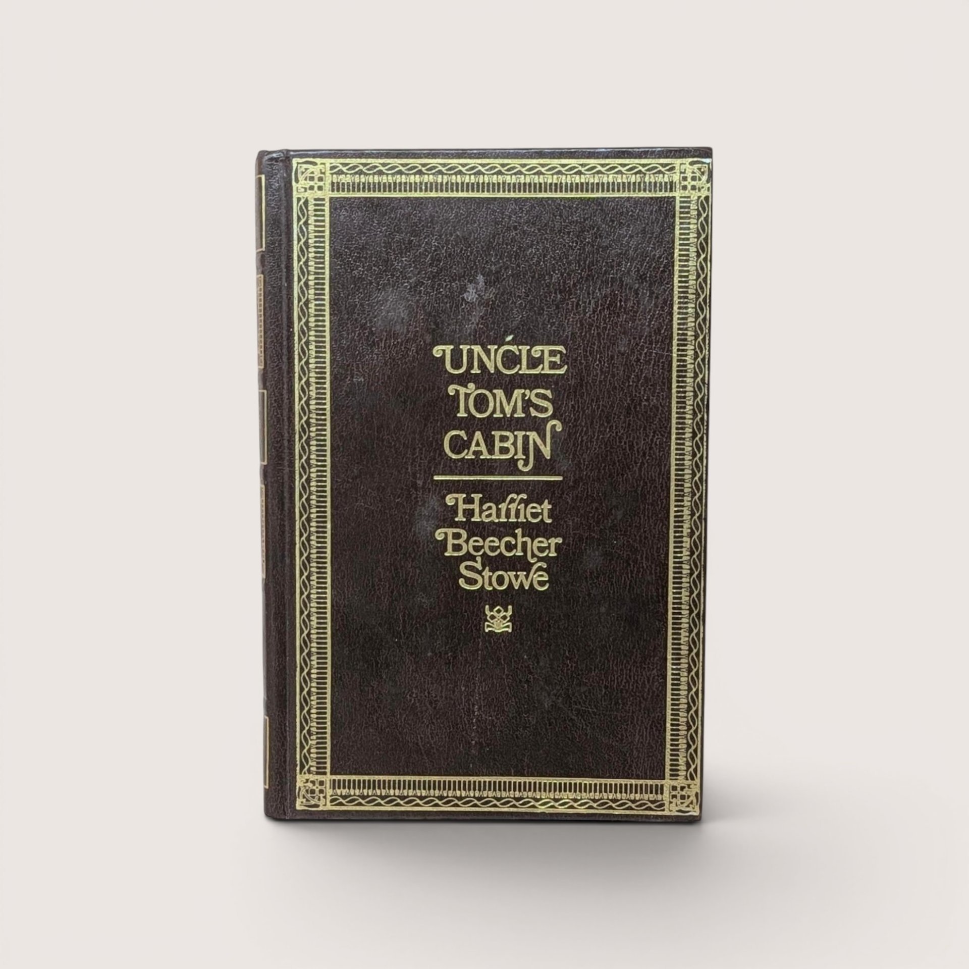 A 1976 hardcover edition of Uncle Tom's Cabin by Harriet Beecher Stowe with a dark brown textured cover and gold gilt lettering and borders