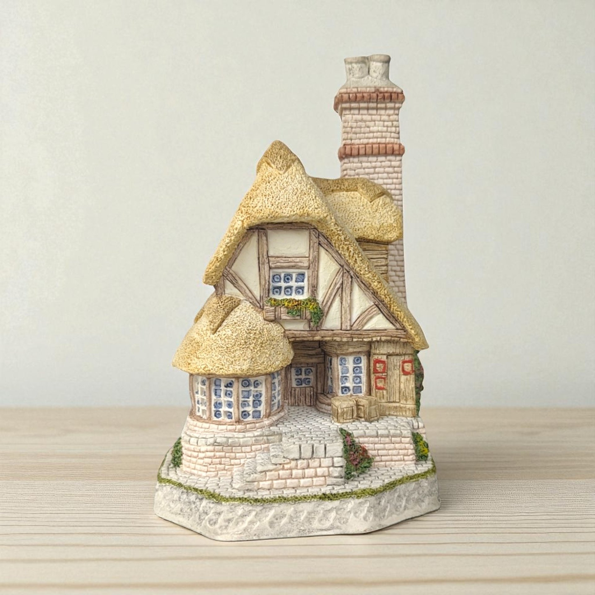 A highly detailed David Winter miniature sculpture of a two-story timber-framed cottage with a thick thatched roof, cobblestone base, stone chimney, and hand-painted floral accents.