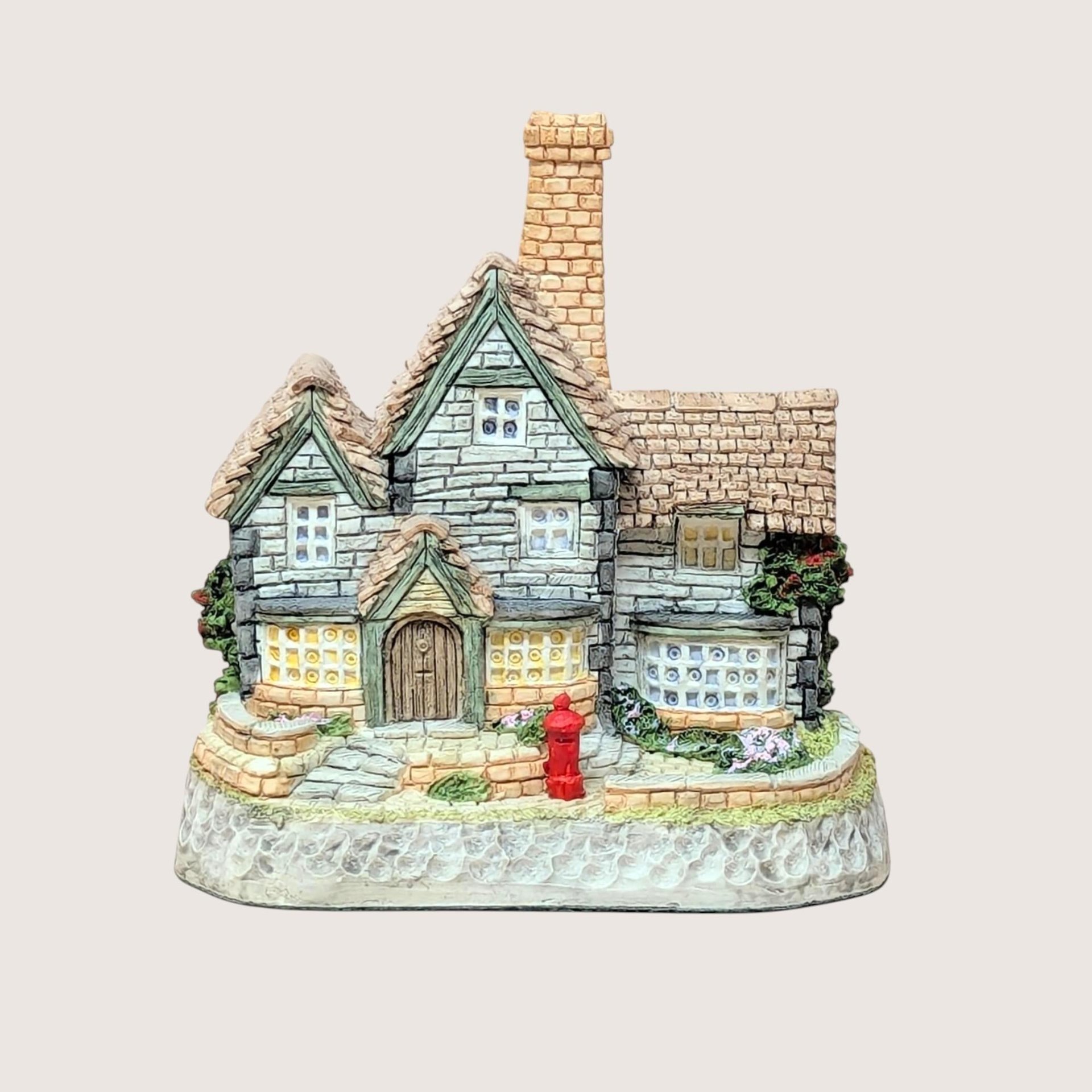 A vintage David Winter miniature sculpture of a British post office featuring a red post box out front and a tall tan chimney