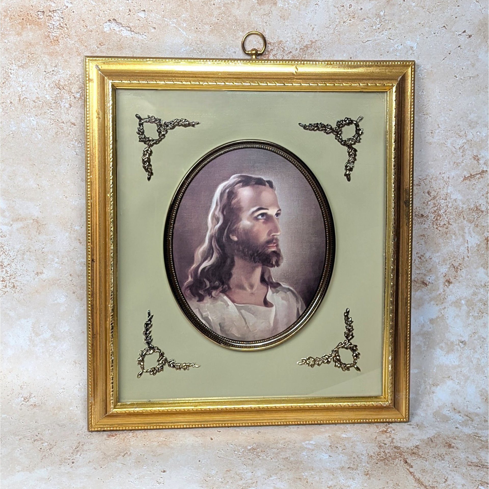 A vintage Turner Manufacturing framed picture of the Head of Christ on a tan textured background. The mid-century print is set within a sage green mat with brass corner filigree and a classic molded gold wood frame with a top hanging loop.