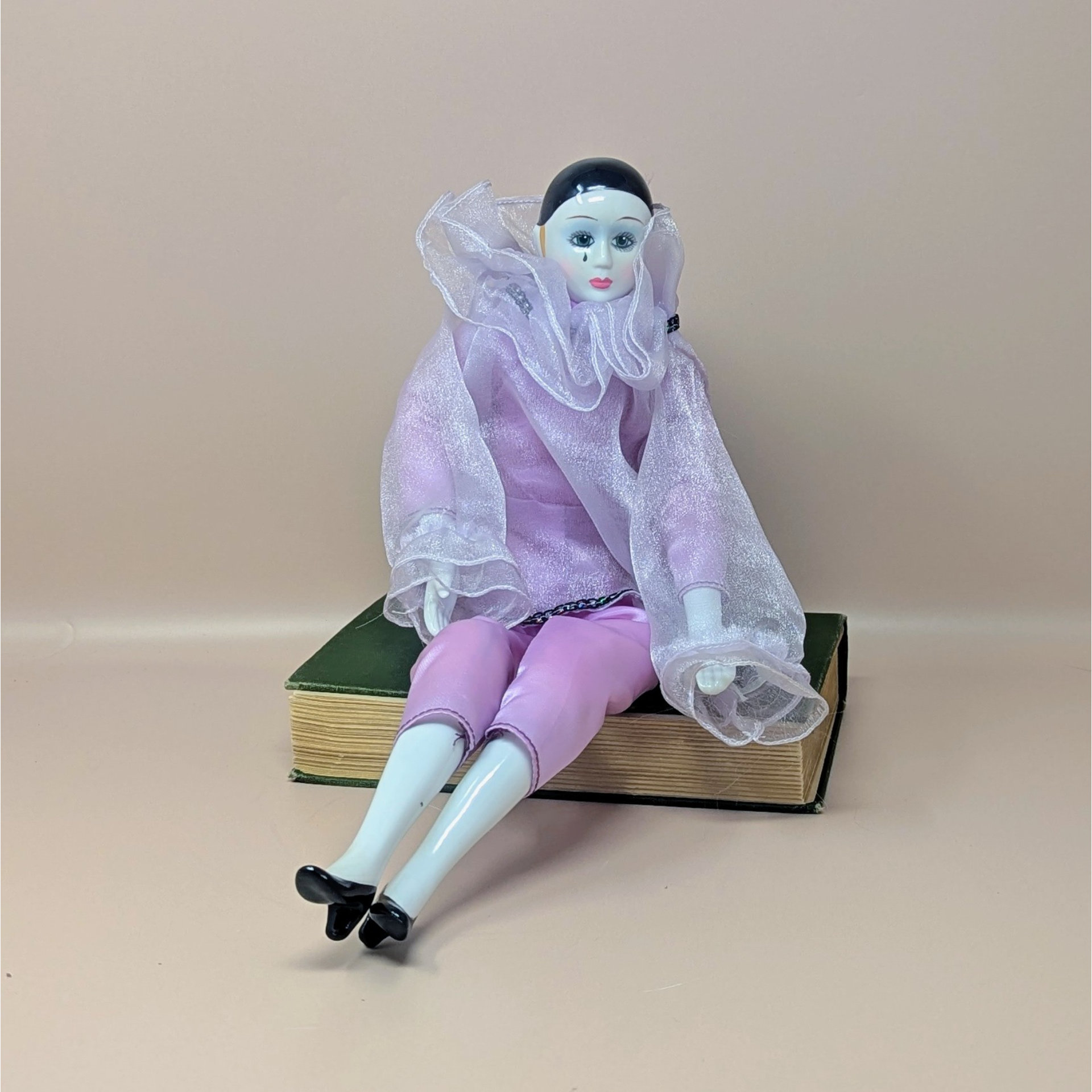 A 16-inch vintage Pierrot clown doll wearing a pink satin and sheer organza outfit, sitting on a green book against a neutral background.