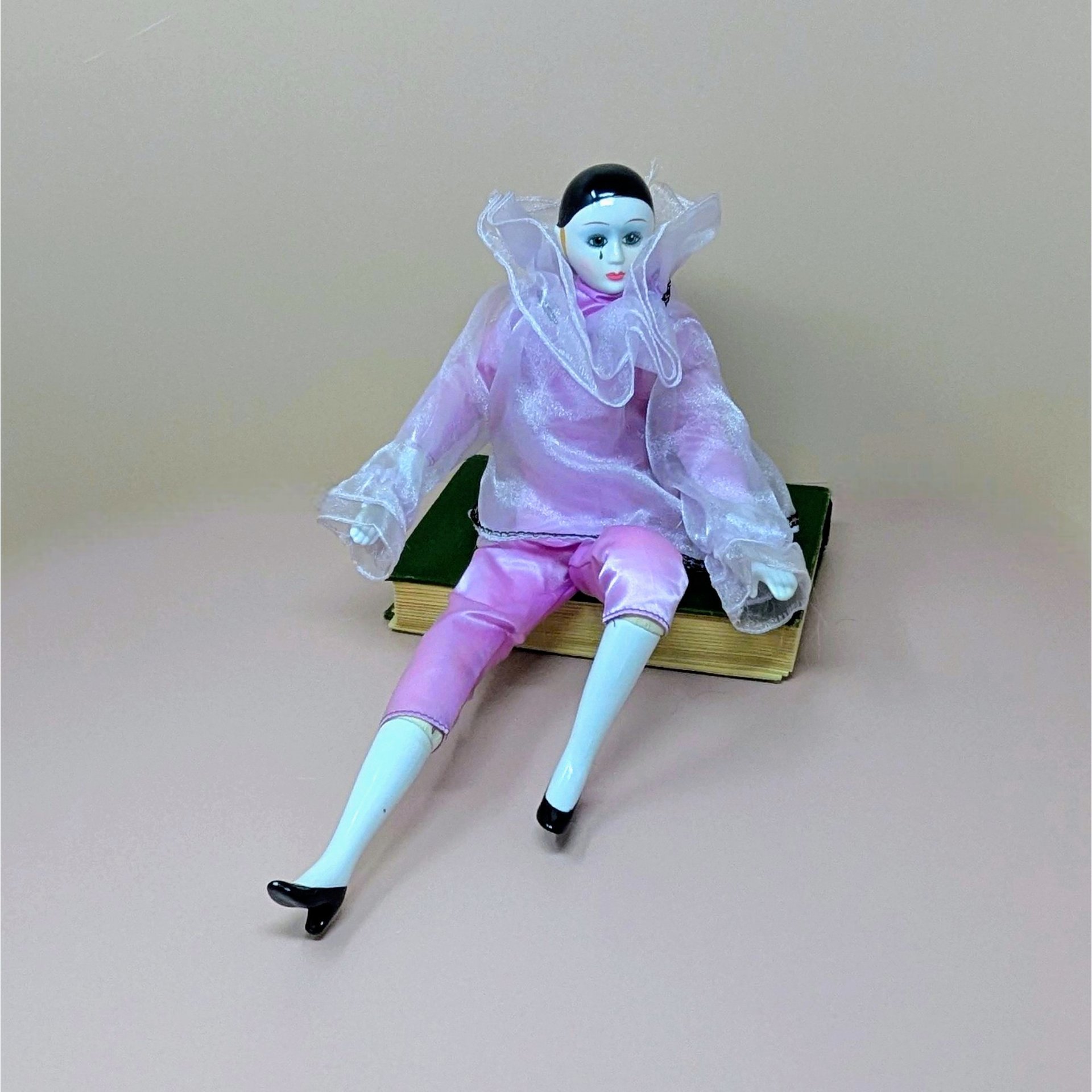 A 16-inch vintage Pierrot clown doll wearing a pink satin and sheer organza outfit, sitting on a green book against a neutral background.