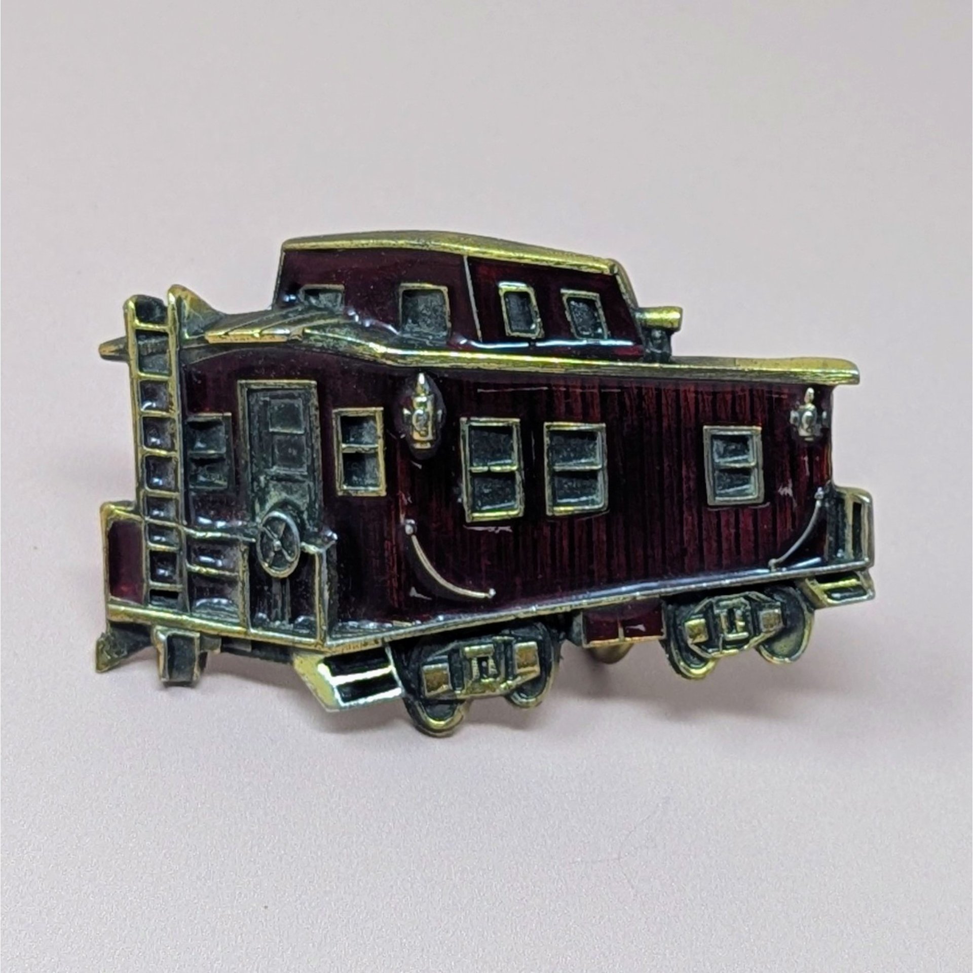 A vintage 1976 belt buckle shaped like a train caboose with deep red enamel and brass-toned metal accents on a neutral background.