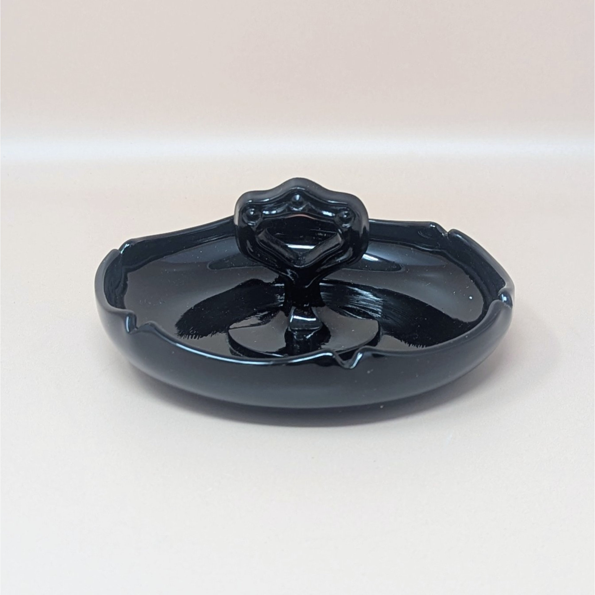 Glossy black amethyst glass trinket dish with a scalloped perimeter and a unique, ornate center handle featuring circular cutouts. The deep violet undertones are visible only under intense light.