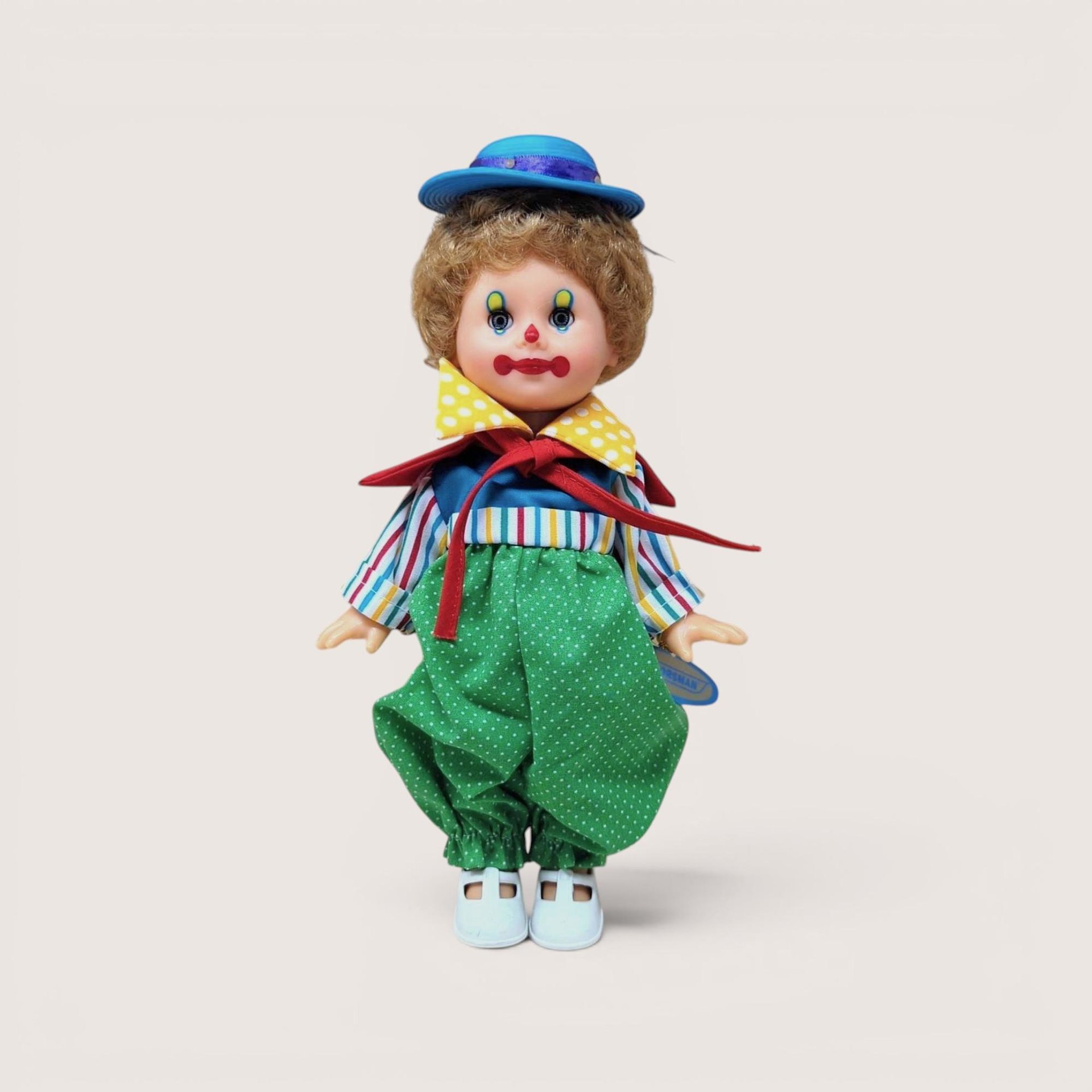 A vintage 10-inch Horsman clown doll with brown hair and a blue hat wearing a colorful mismatched outfit of stripes and polka dots against a neutral background.