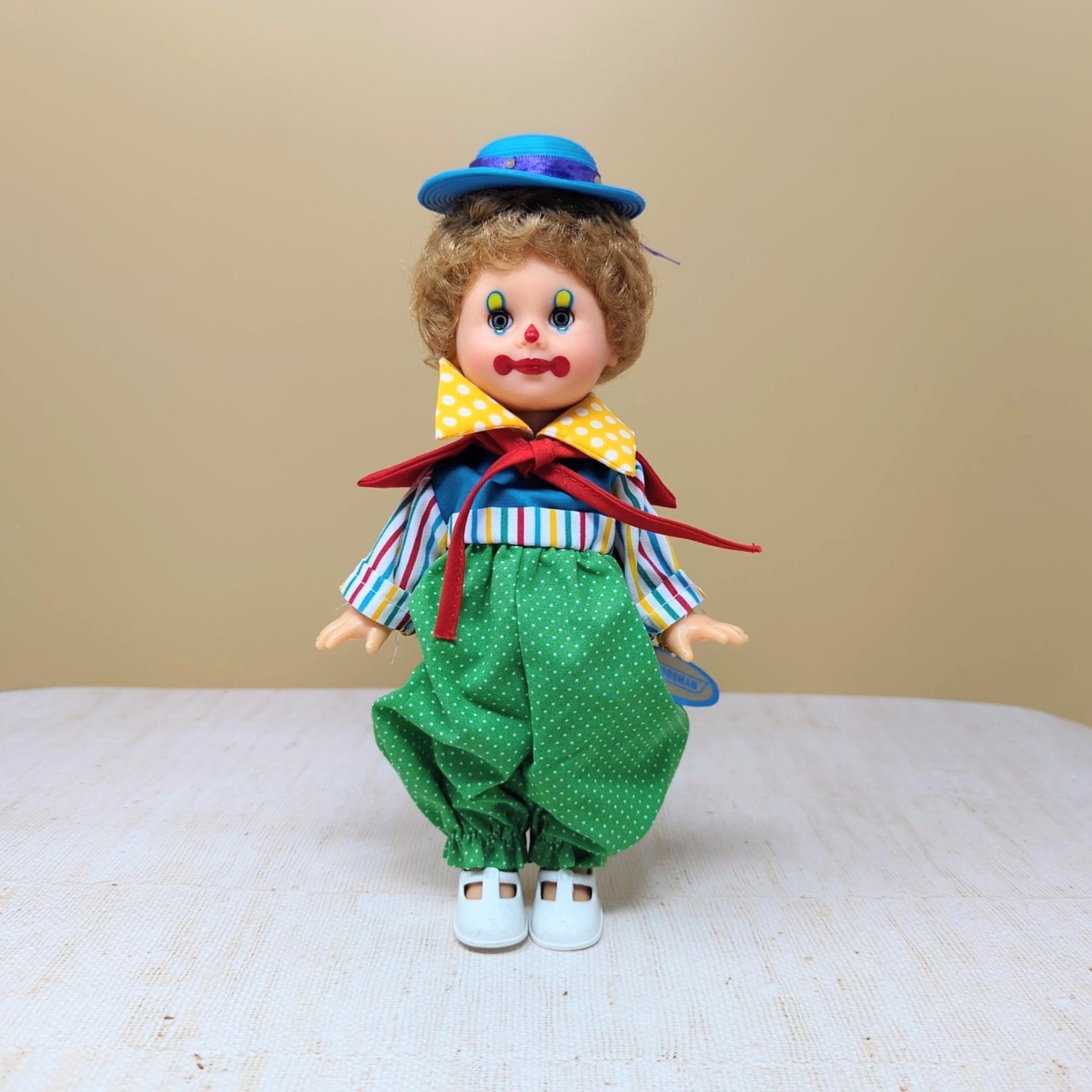 A vintage 10-inch Horsman clown doll with brown hair and a blue hat wearing a colorful mismatched outfit of stripes and polka dots against a neutral background.