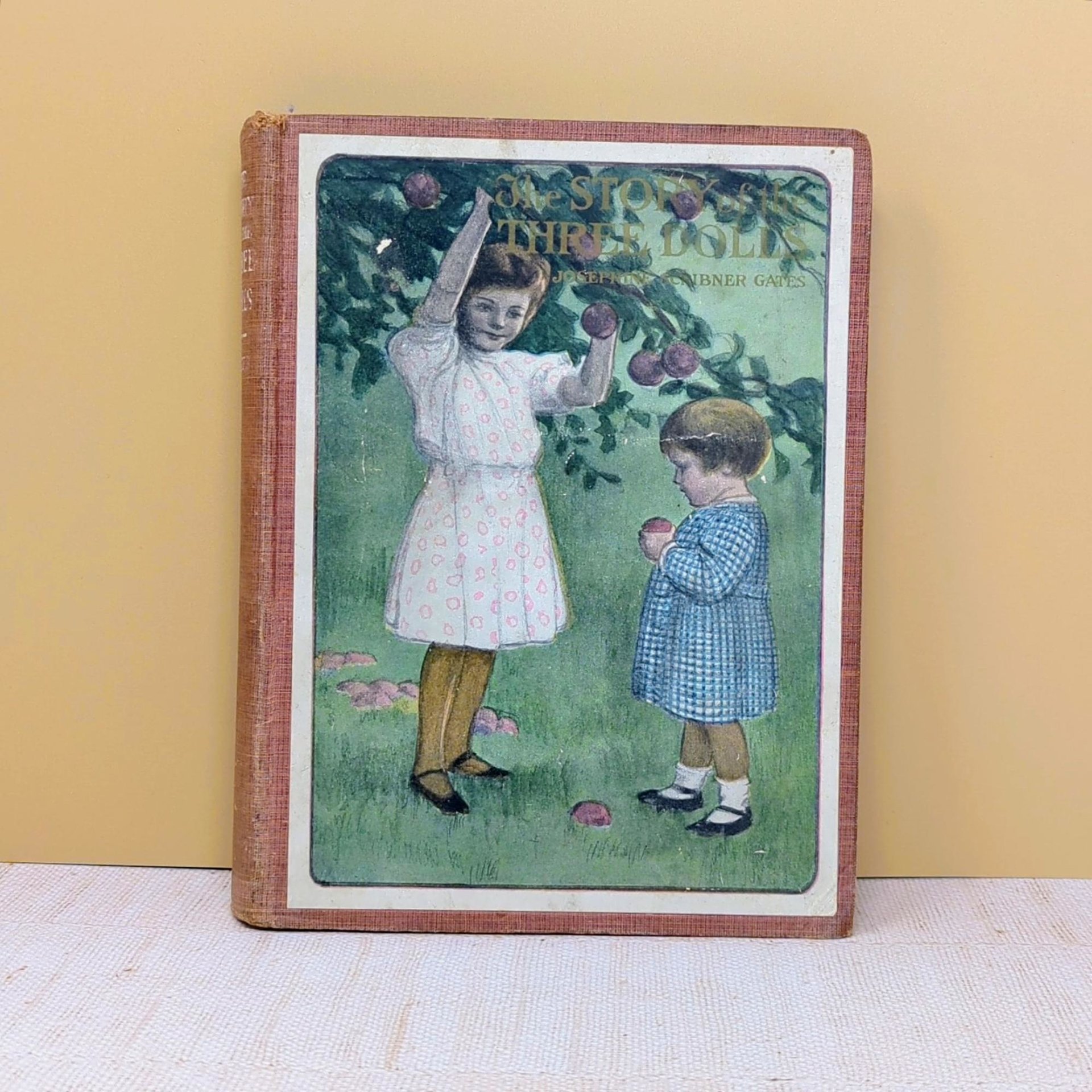 An antique children's book with a large color lithograph pastedown on the front cover depicting two young girls in an orchard against a neutral background.