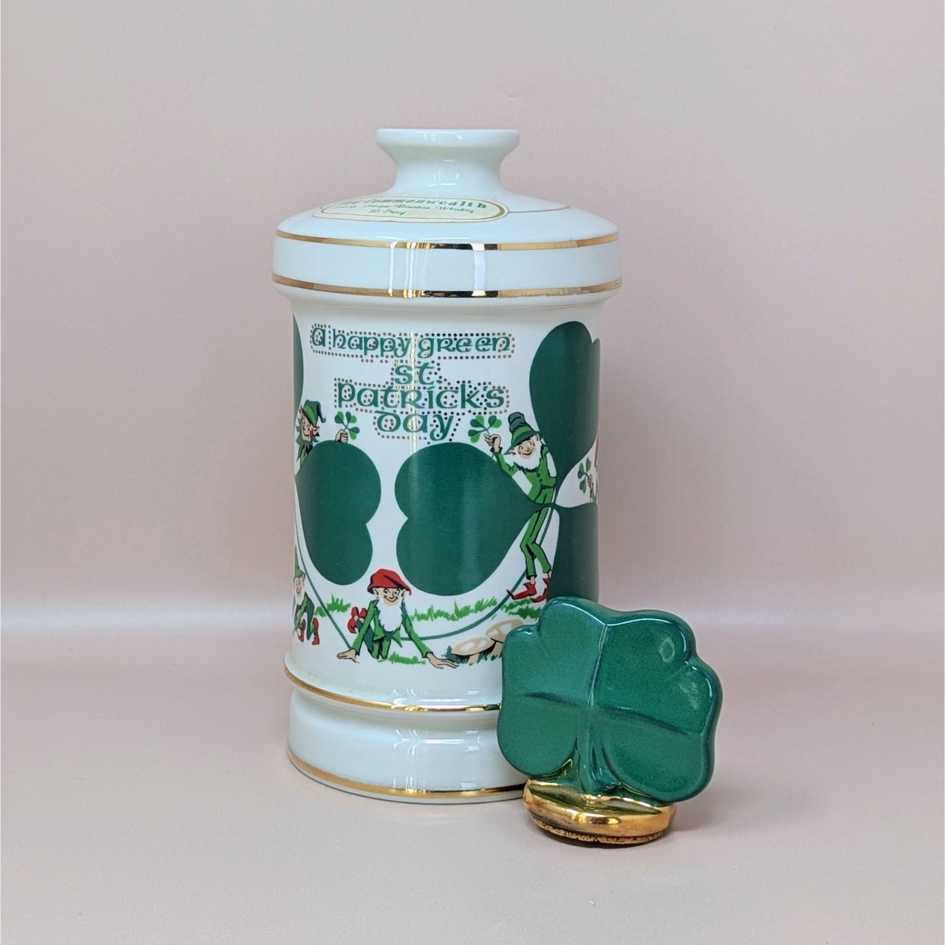 A tall white porcelain decanter featuring green "A Happy Green St. Patrick’s Day" typography, leprechaun illustrations, and a gold-trimmed shamrock stopper against a neutral background.