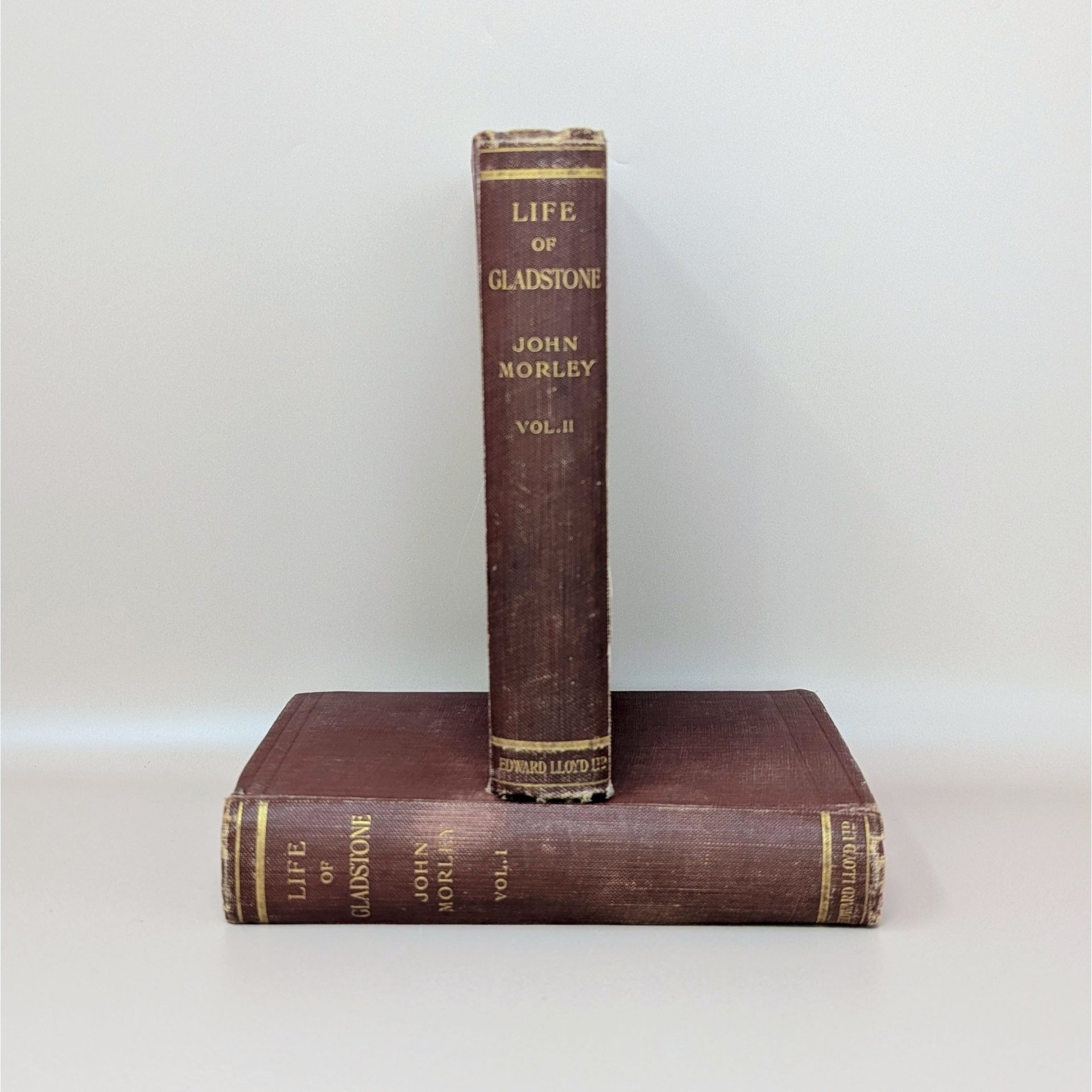 Two antique burgundy cloth-bound books stacked horizontally, showing gilded spine titles for The Life of Gladstone by John Morley.