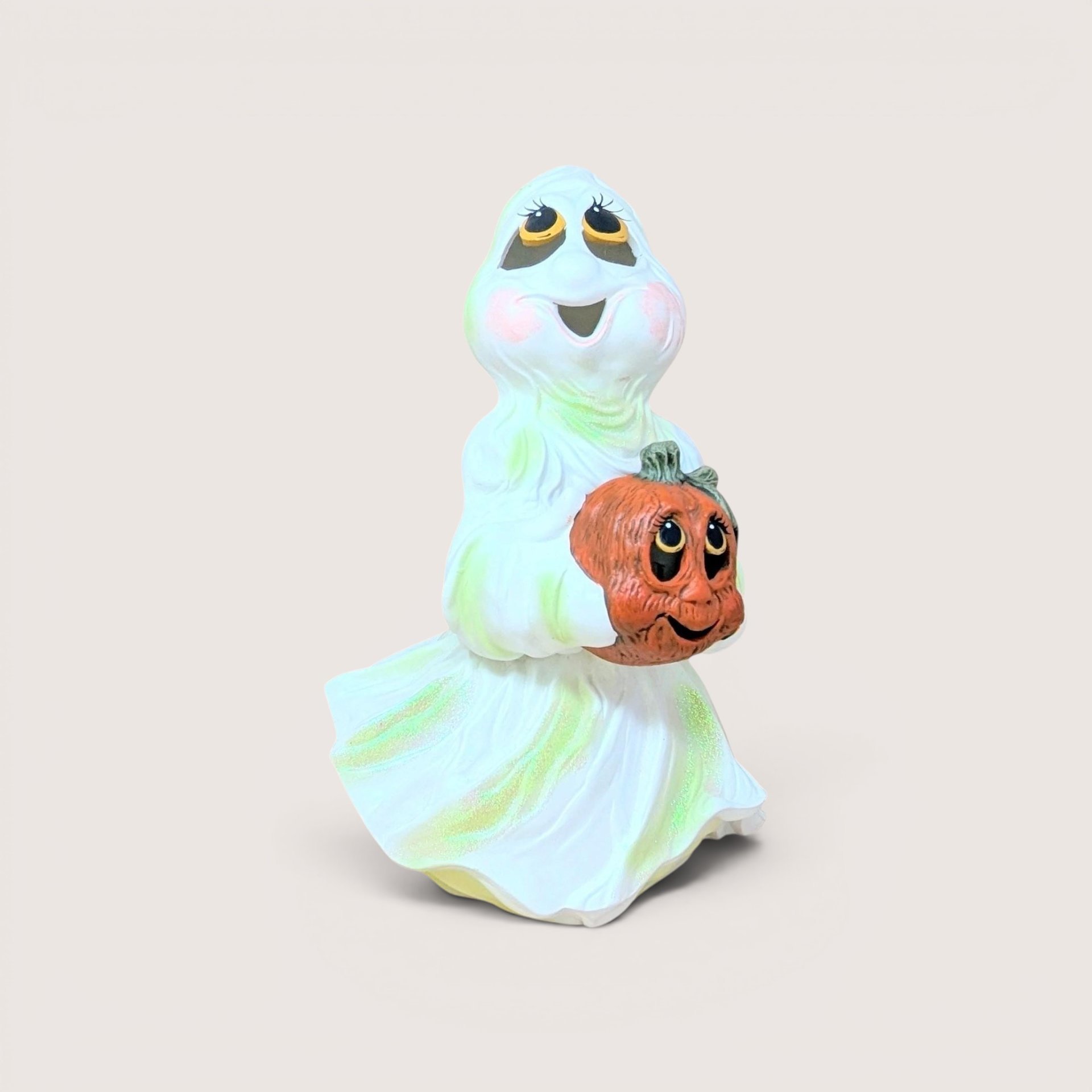 Vintage iridescent ceramic ghost figurine with large eyes, smiling and holding a jack-o'-lantern pumpkin.