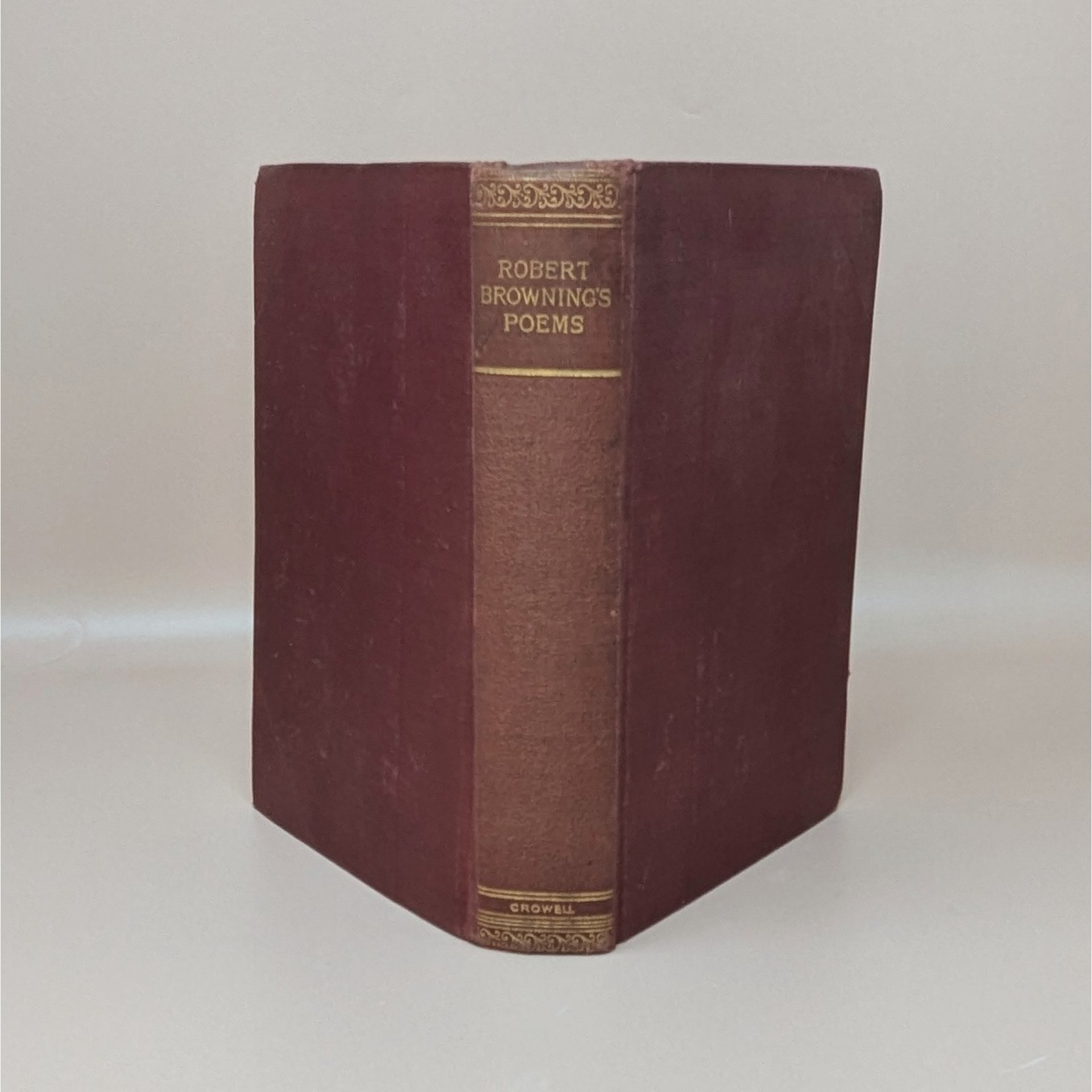 A burgundy cloth-bound hardcover book standing upright, featuring gilded typography on the spine for Robert Browning's Poems against a neutral background.